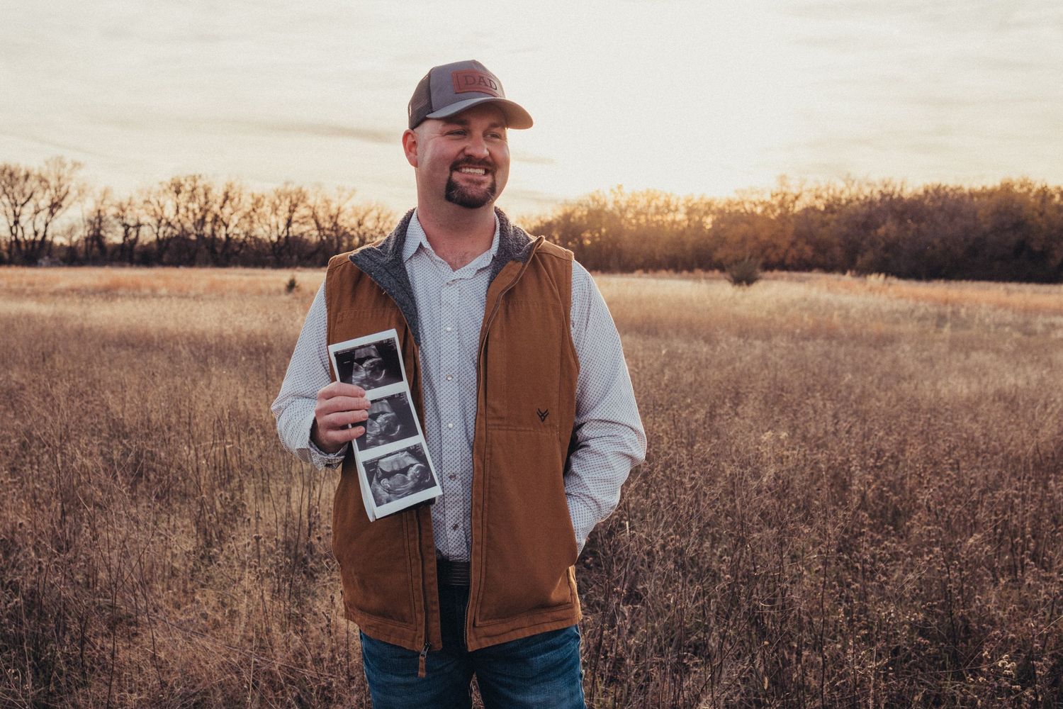 Couple holding ultrasound photos during outdoor pregnancy announcement shoot.