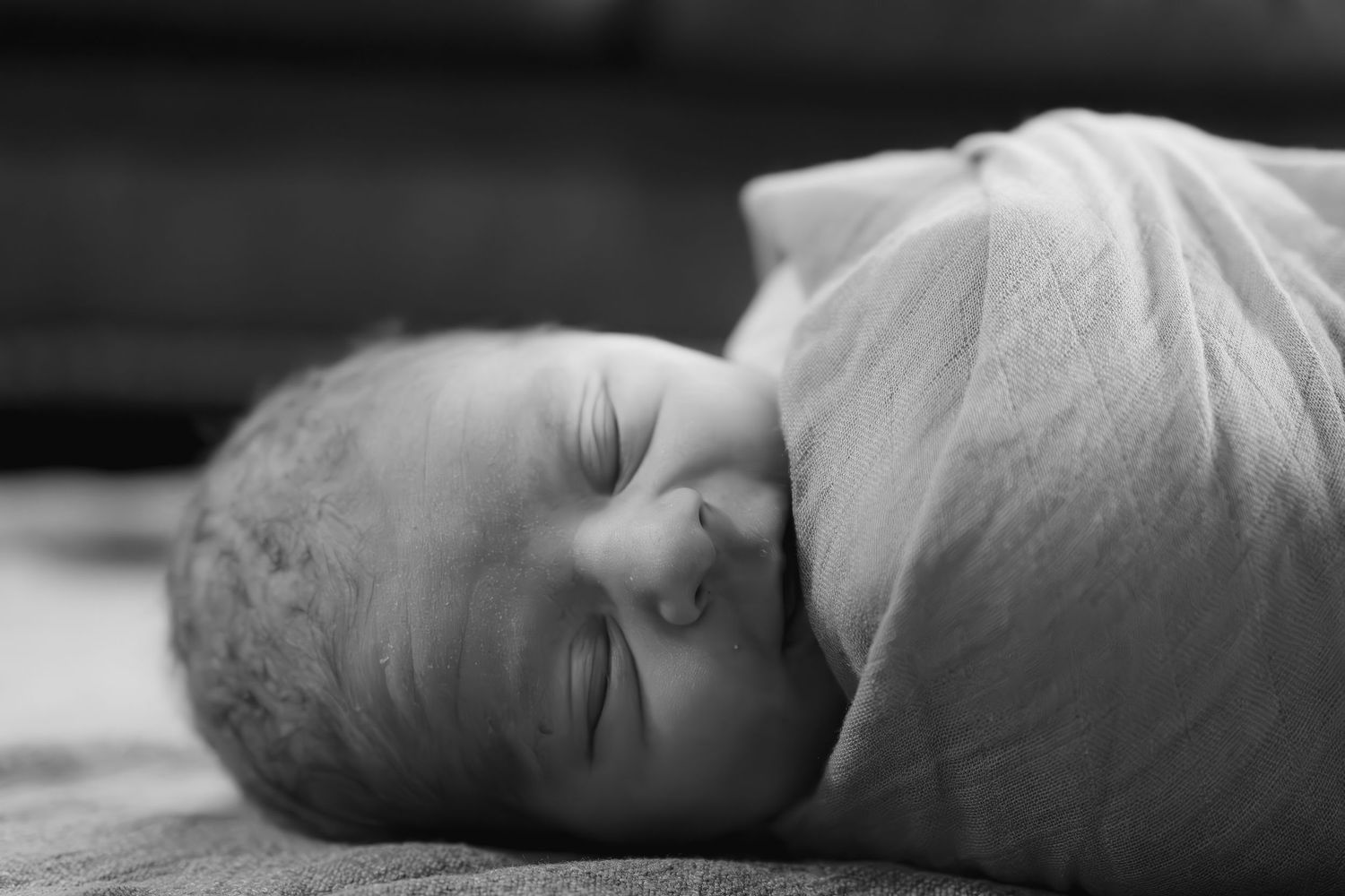 Peaceful sleeping newborn baby wrapped in white blanket.
