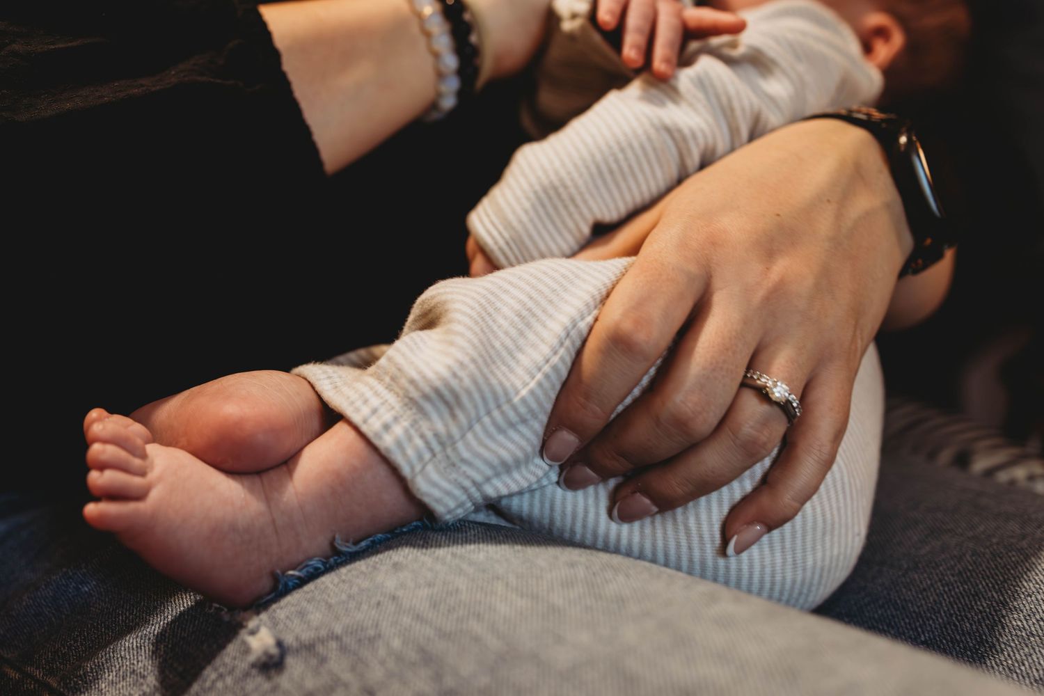 Close up of tiny baby feet and hands with adult hand providing gentle touch.