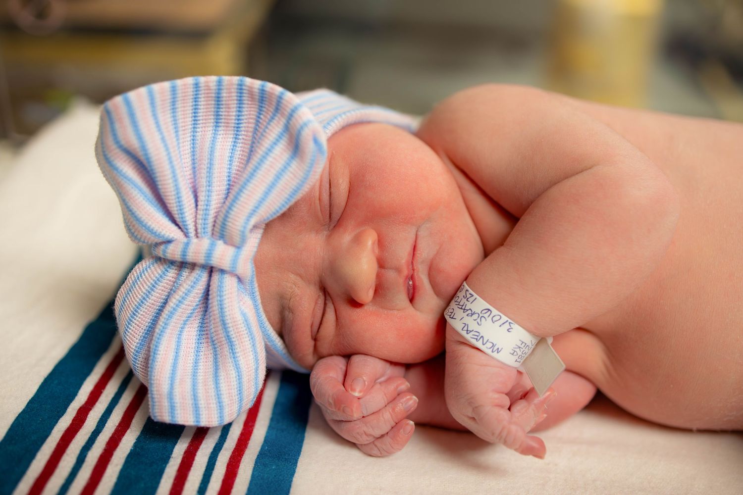 Detailed shot of a sleeping newborn baby's features with striped hospital hat.