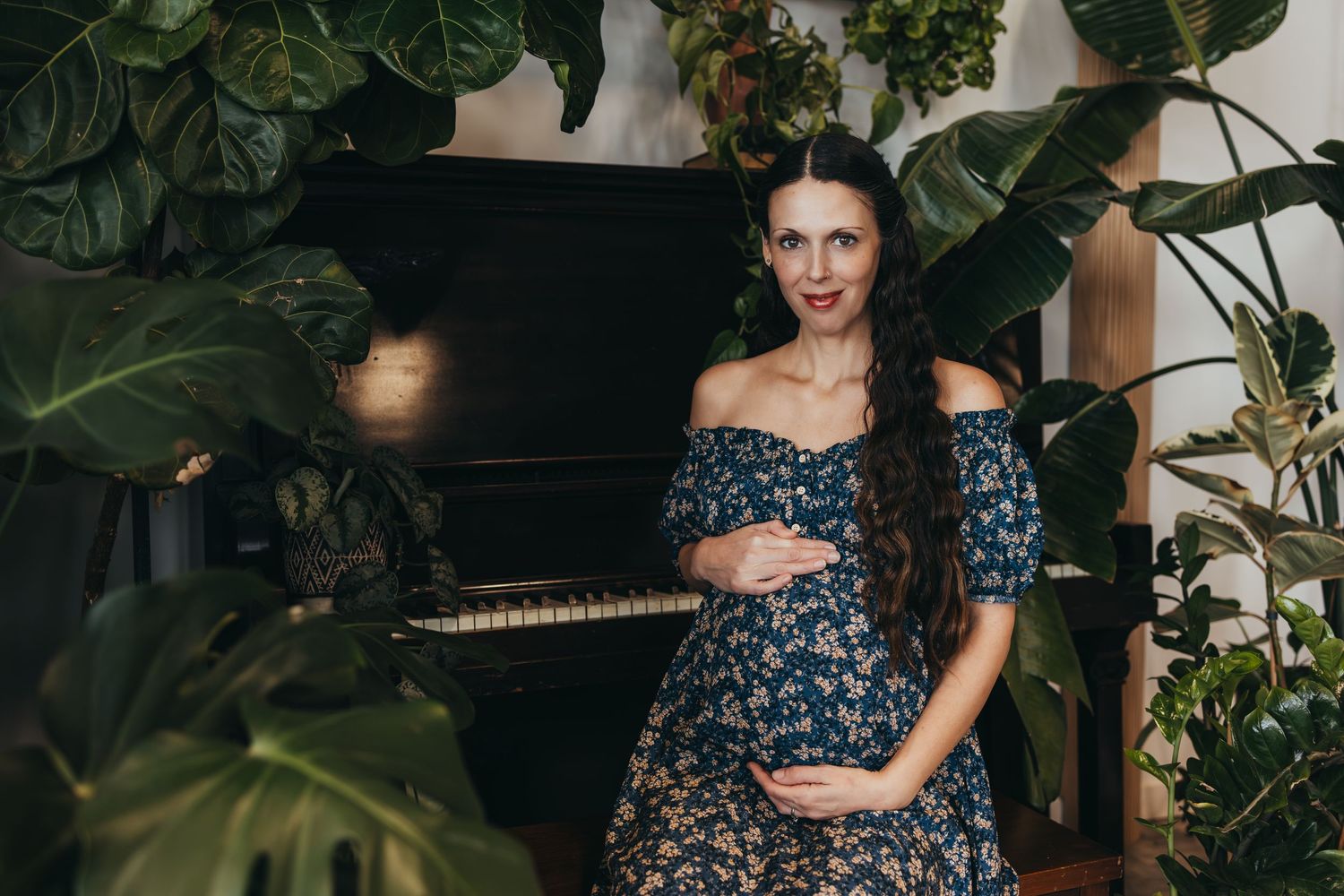 Maternity photo near piano with lush indoor plants and floral dress.
