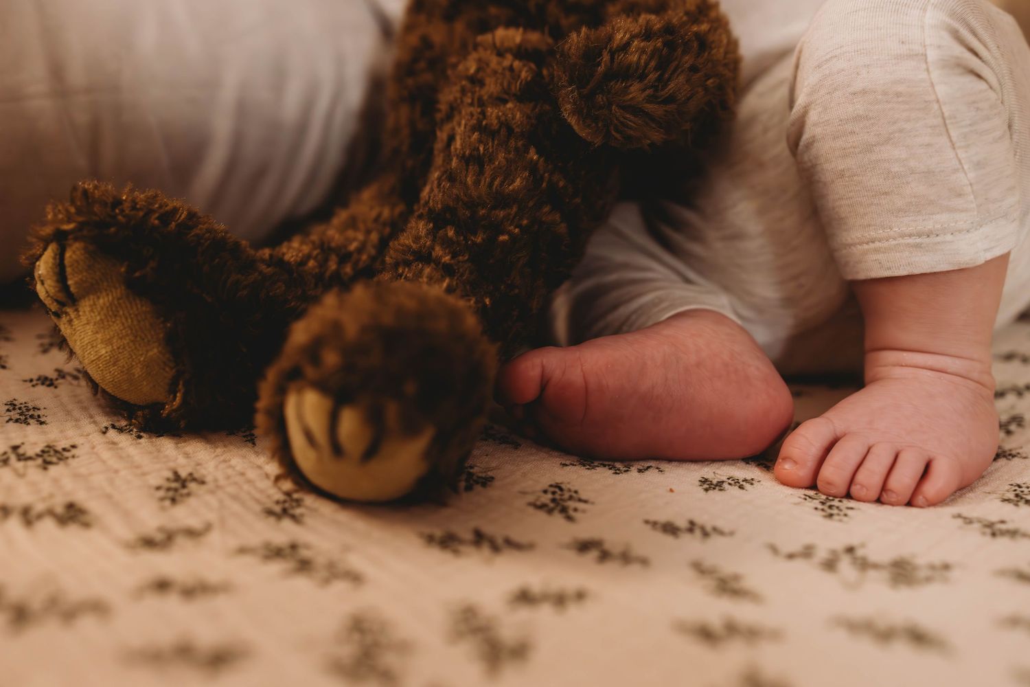 Close-up of a brown teddy bear and bare feet on a patterned bedspread.