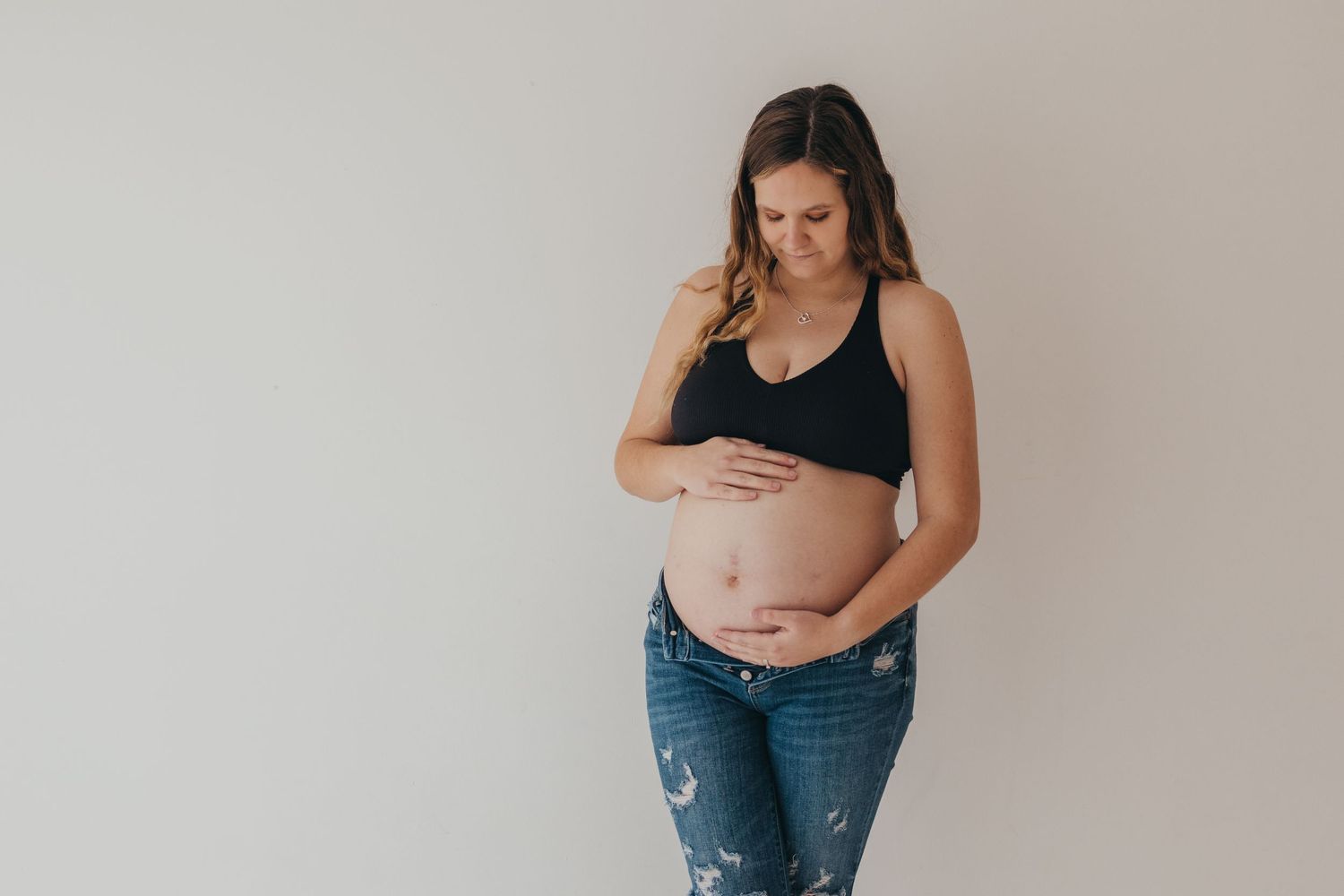 A series of five maternity photos showing a pregnant woman in jeans and black top against a neutral background.
