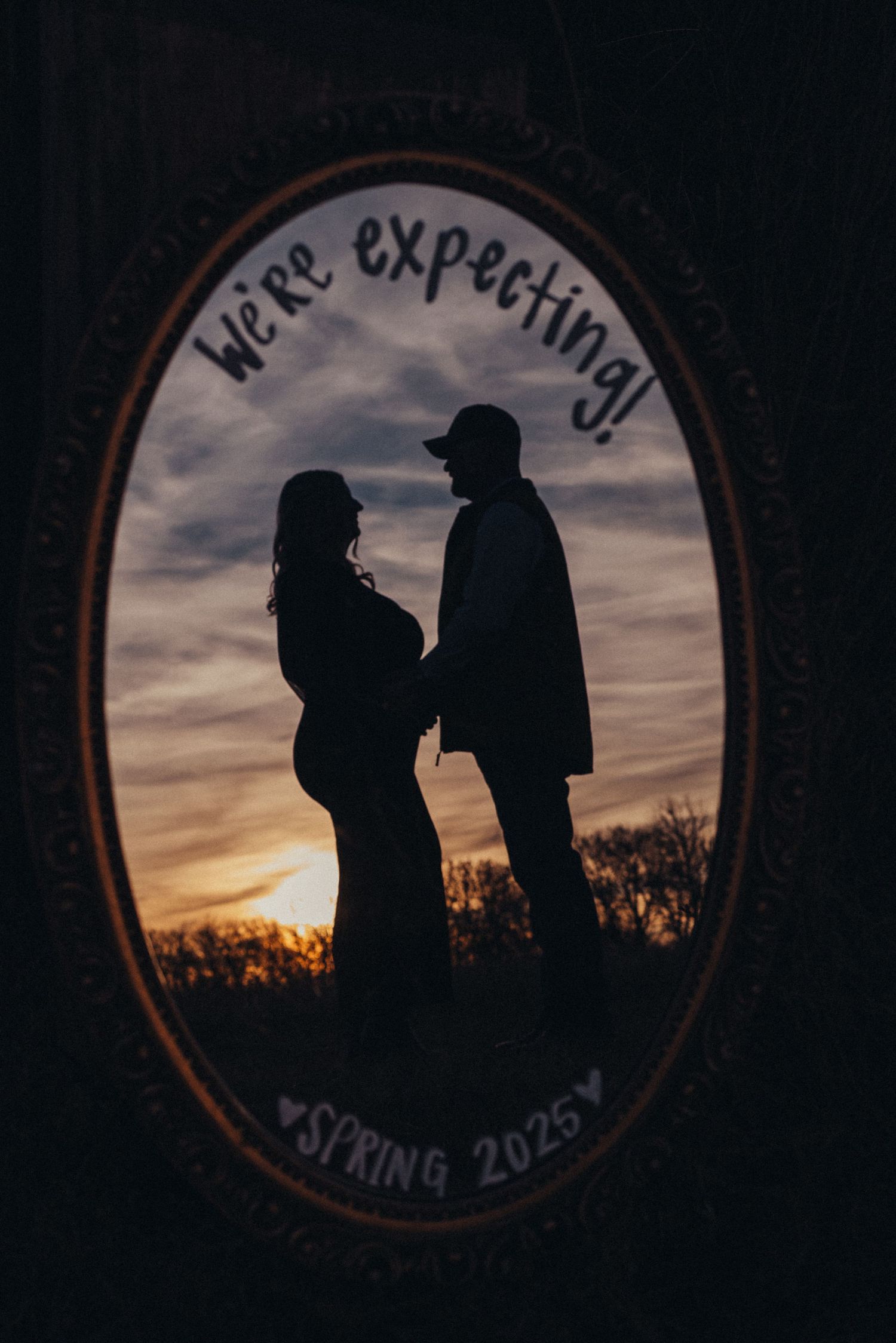 Silhouettes of two people stand against a dramatic sunset sky framed in a circular window.