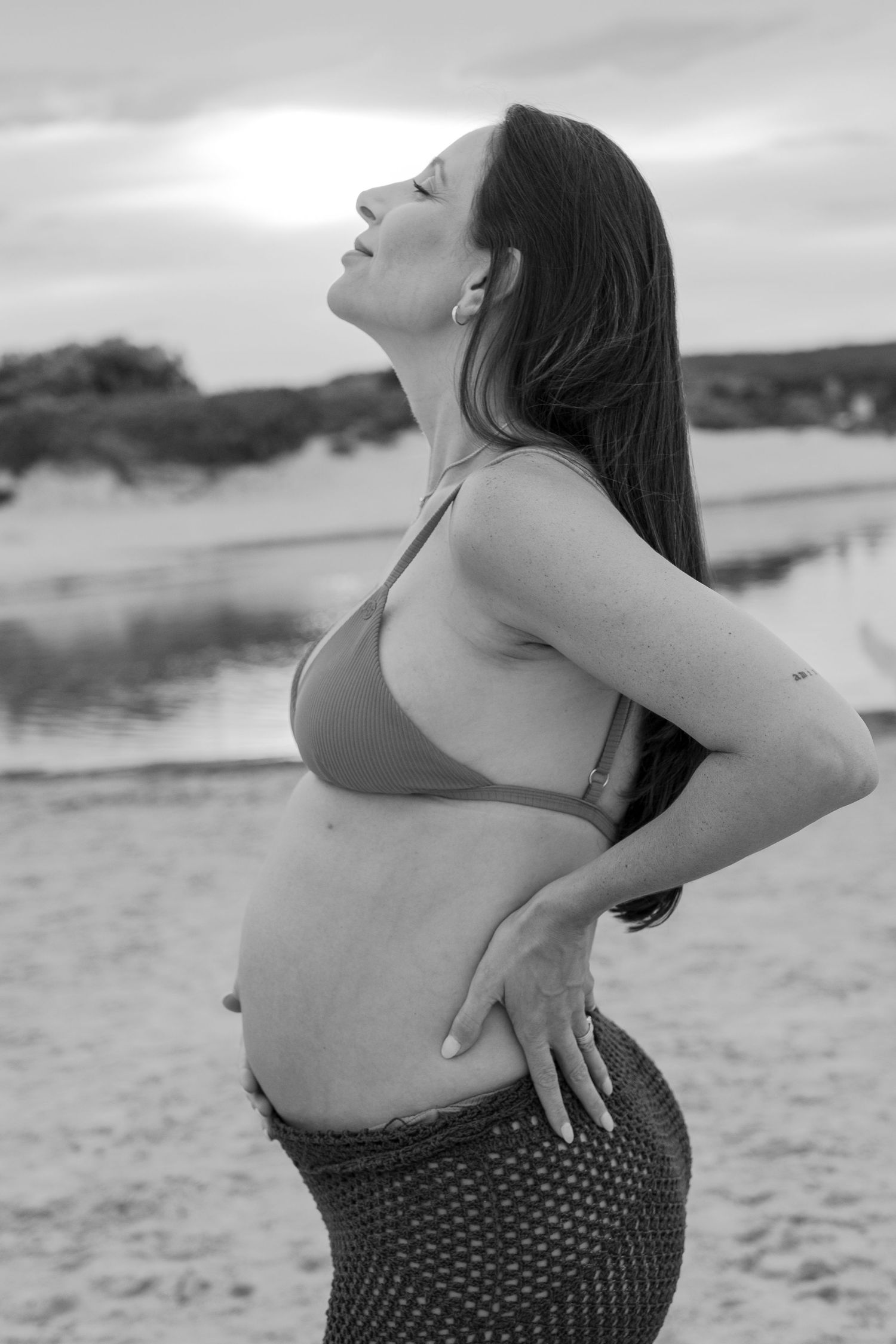 Woman in polka dot swimsuit poses expressively on beach in black and white series.