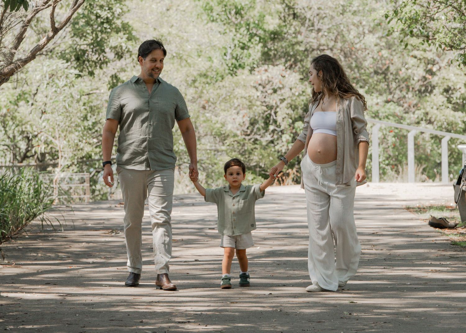 Family walking hand in hand down a sunlit garden path surrounded by greenery and trees.