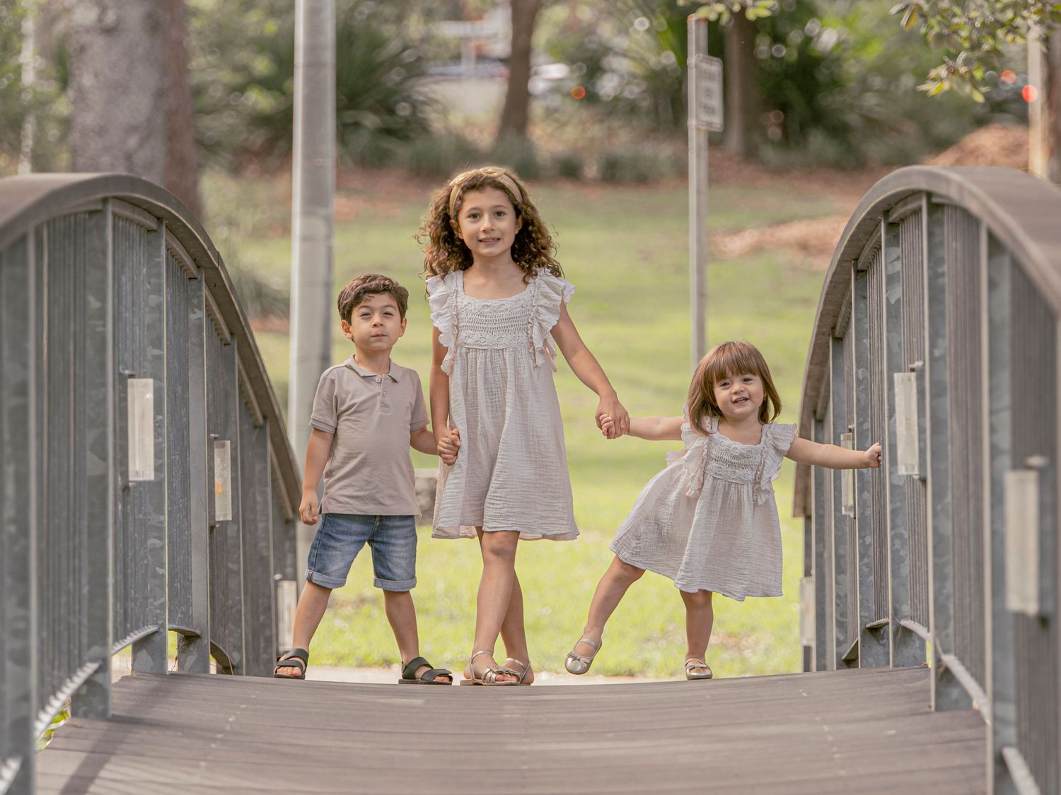 Children play and run together on a wooden bridge in a sunny outdoor park setting.