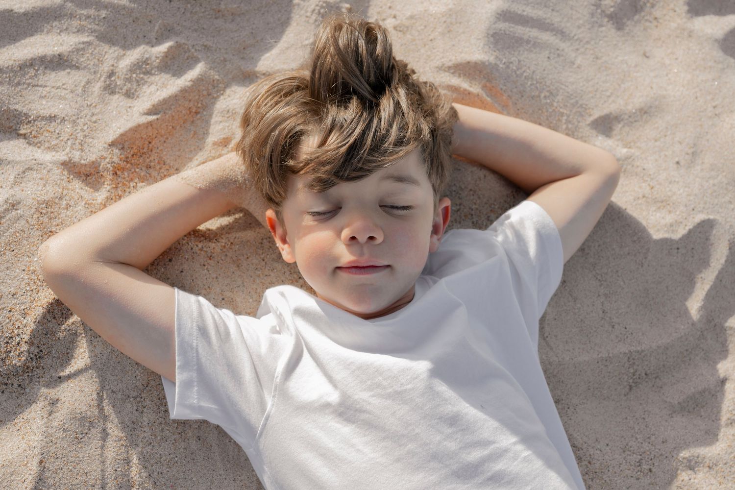 Child laying in sand making beach angels during summer.