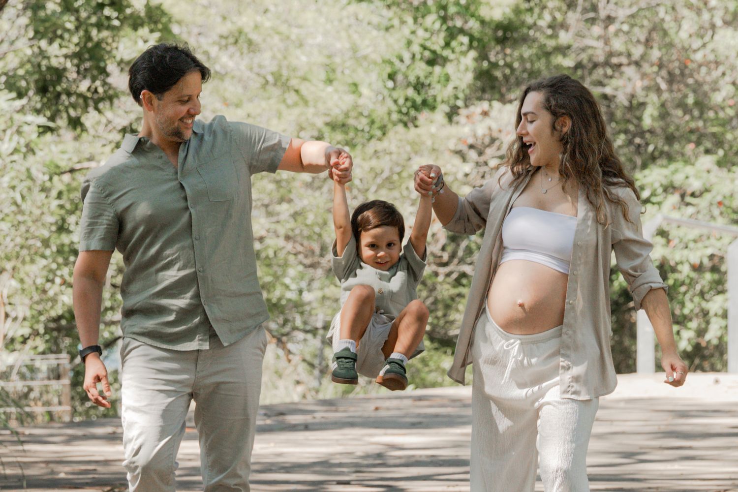 Family enjoying a playful moment together while walking on a tree-lined path in casual summer outfits.