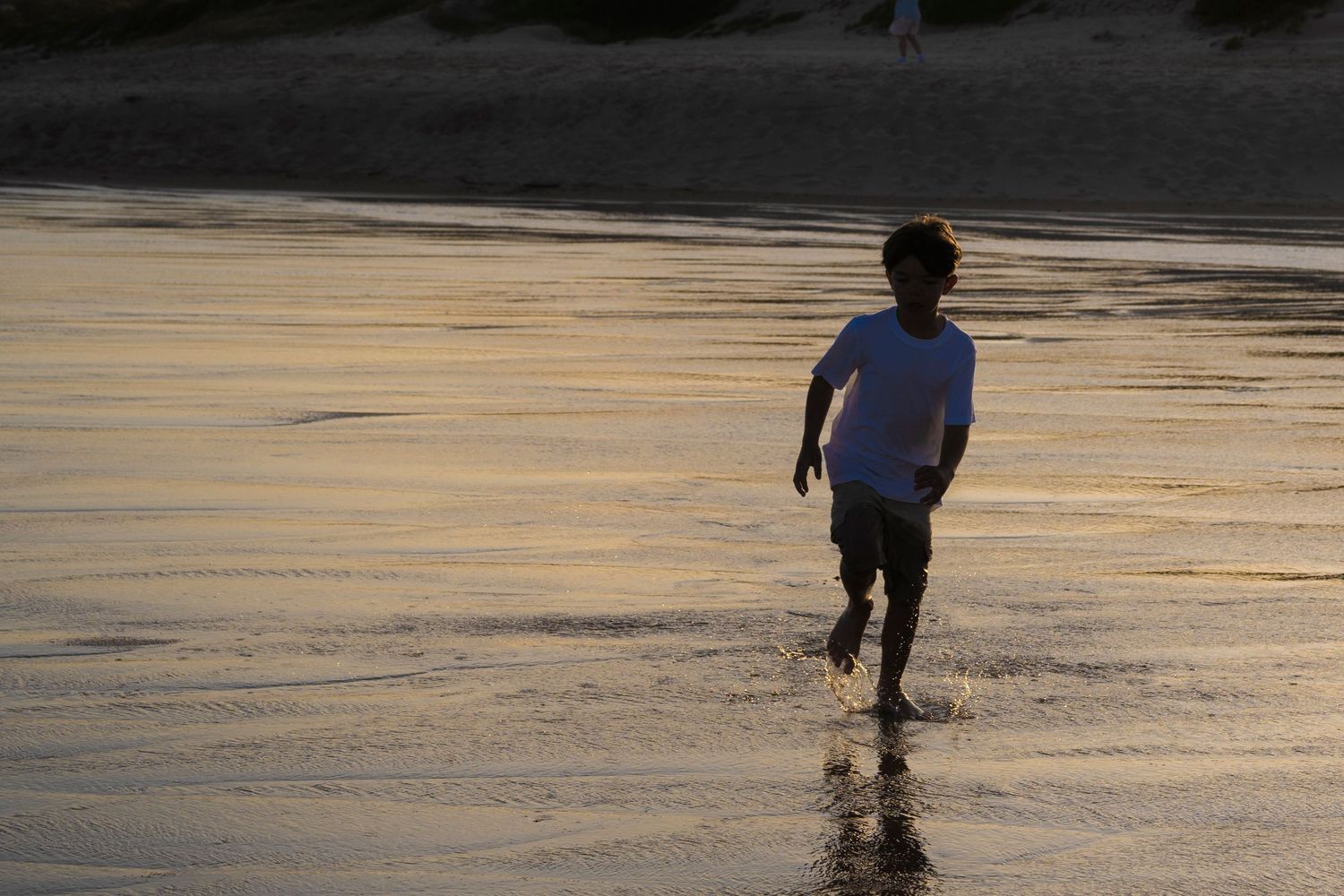Children running on wet sand during sunset at the beach.