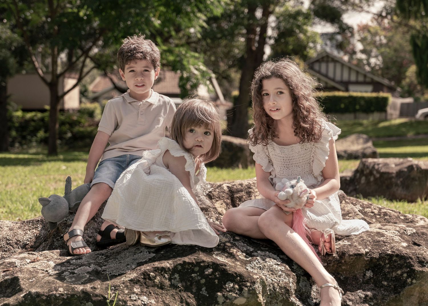 A group sits together on a fallen tree trunk in a sunlit garden setting, creating a warm family moment.