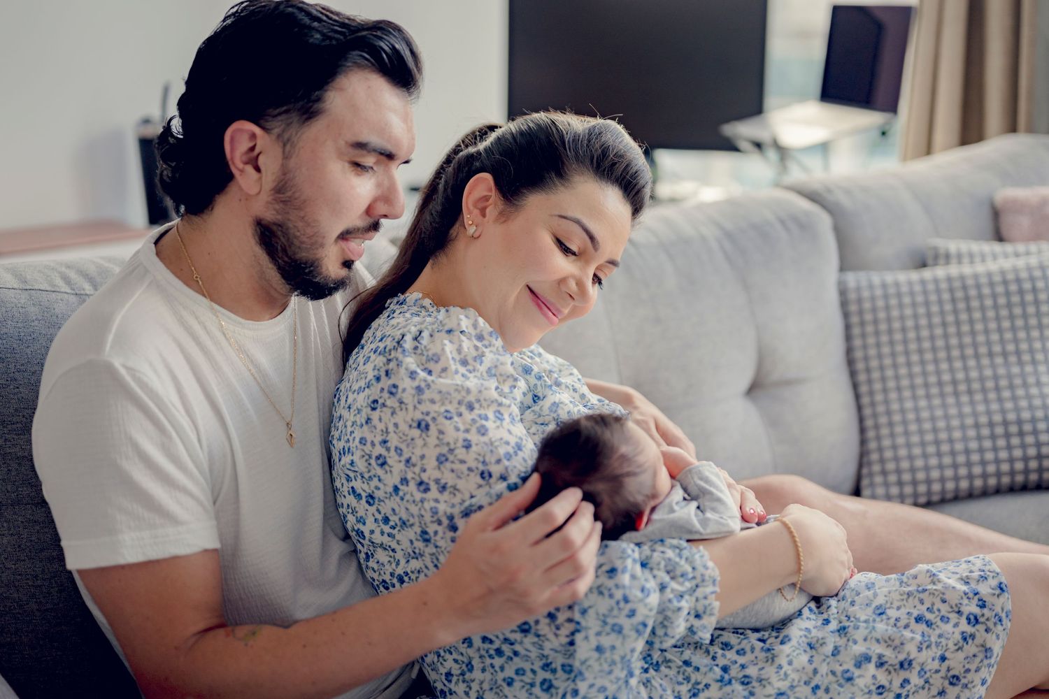 Family moment with parents and newborn relaxing together on a gray couch.