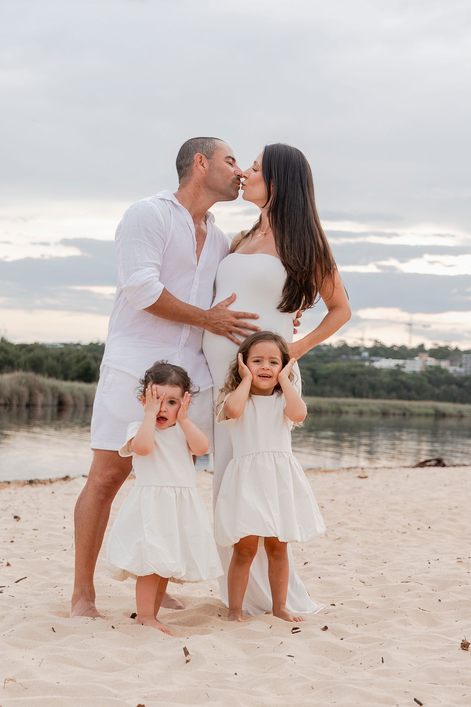 Family beach portrait with playful children in matching white dresses.