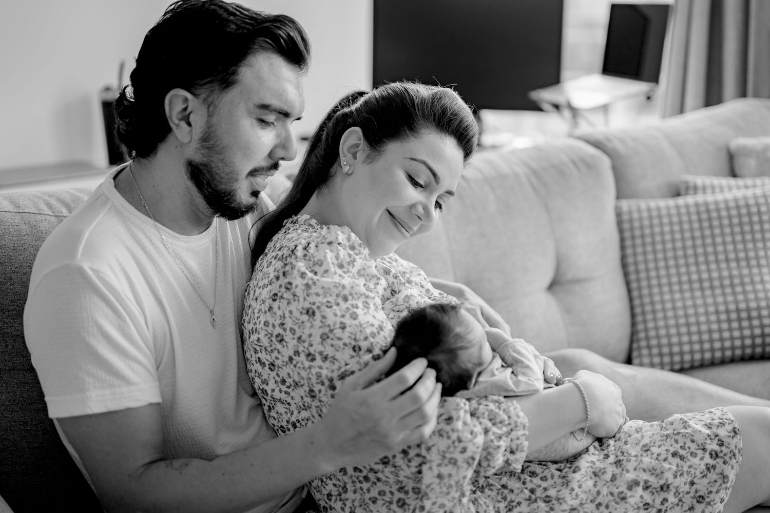 Black and white photo of parents gazing lovingly at their newborn on a couch.