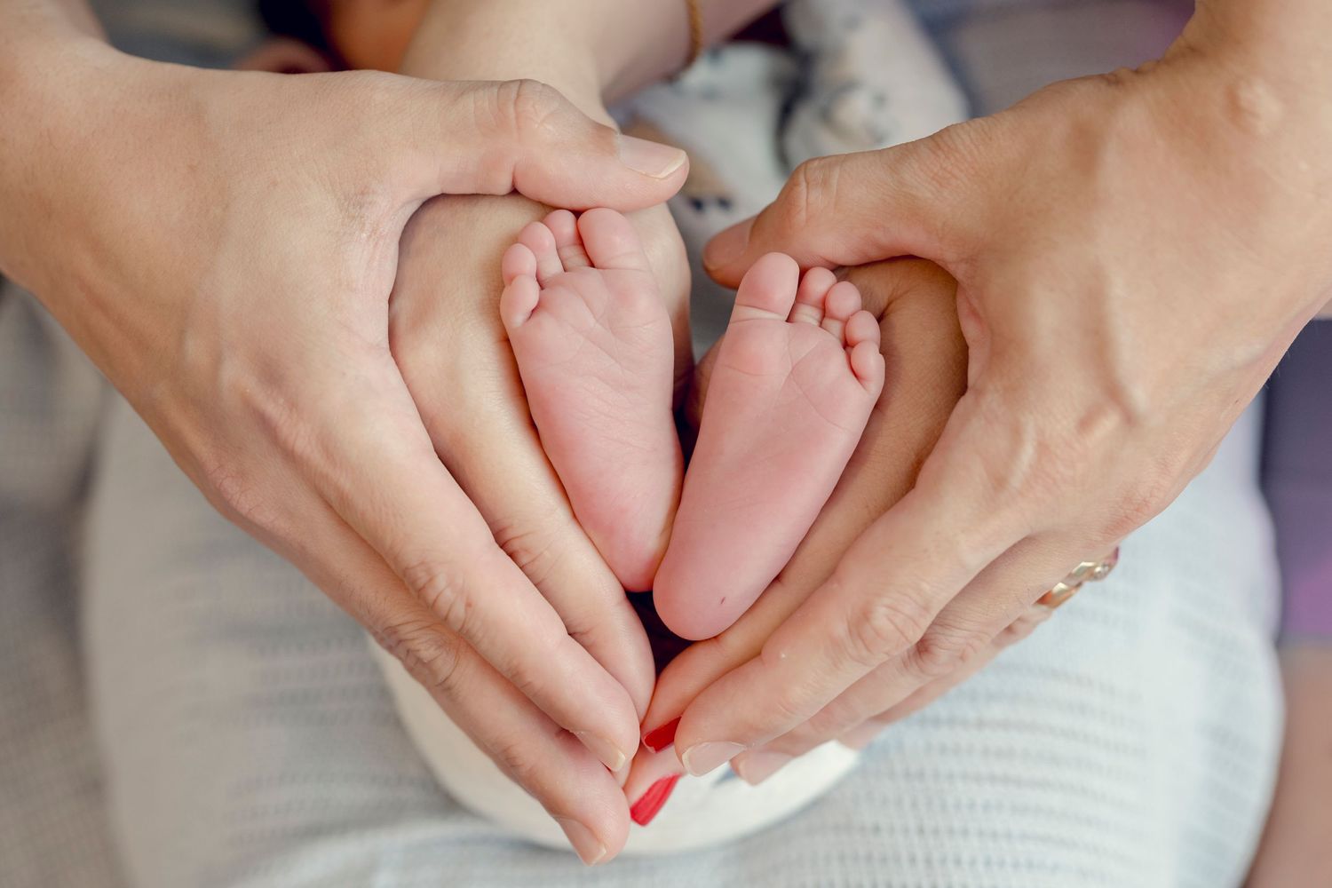 Adult hands forming heart shape around tiny newborn baby feet.