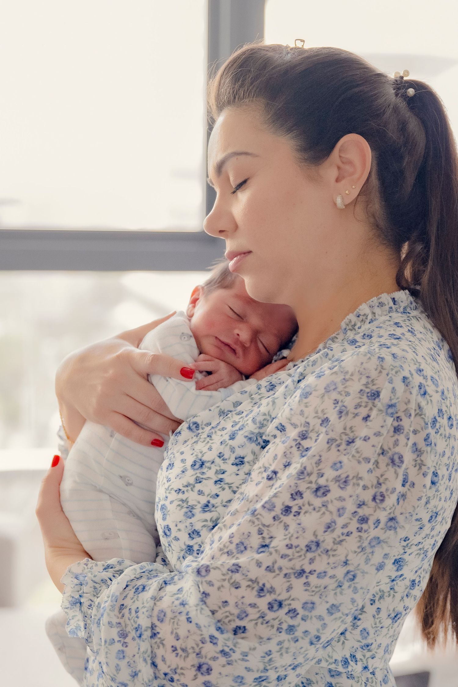Mother in floral dress cradling and kissing her newborn baby.