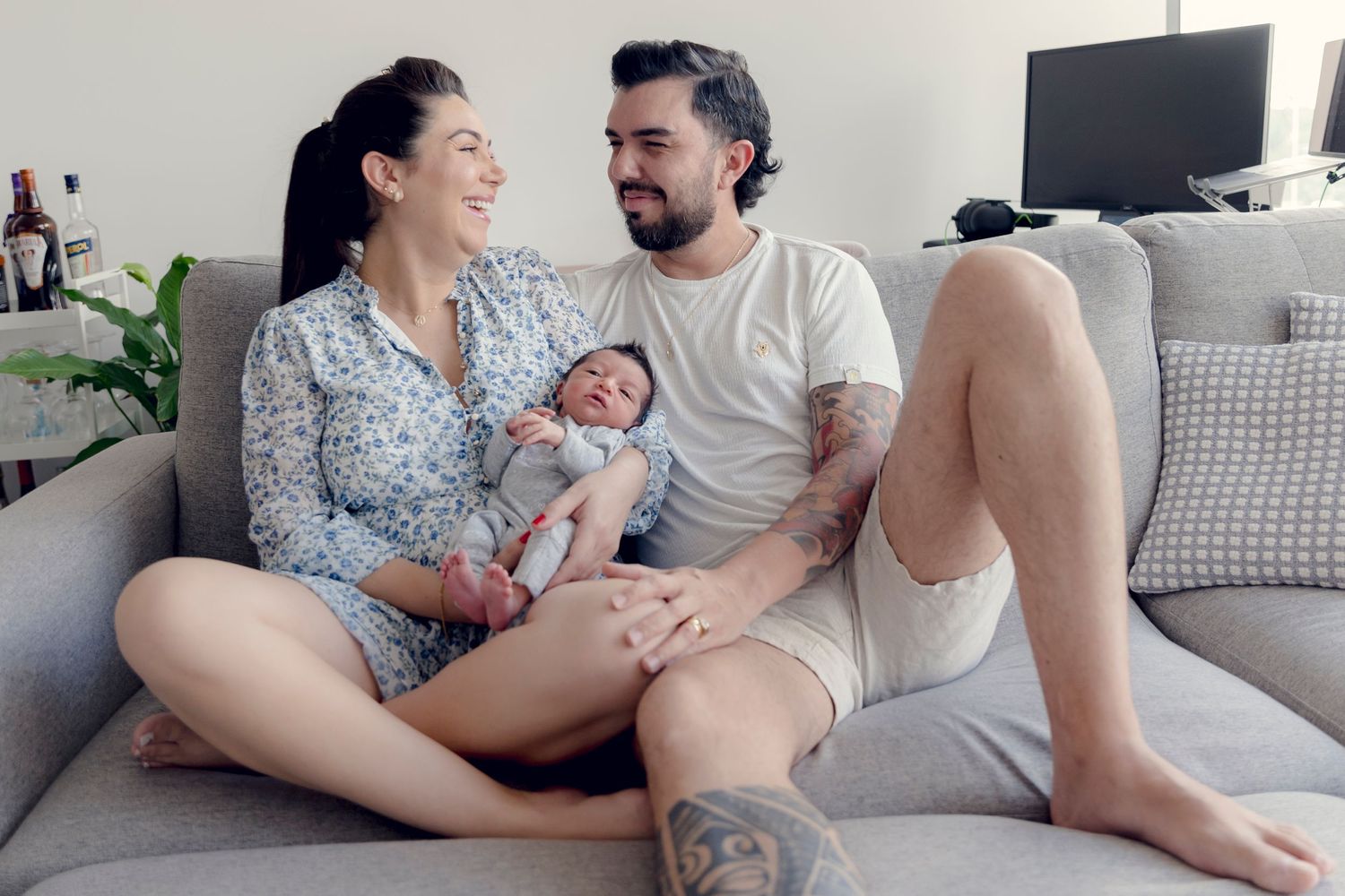 Happy family relaxing on gray couch with their newborn baby.