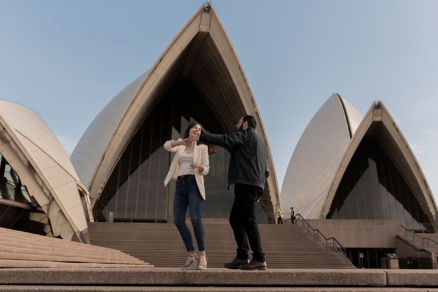 Couple poses playfully in front of the iconic Sydney Opera House sails at sunset.