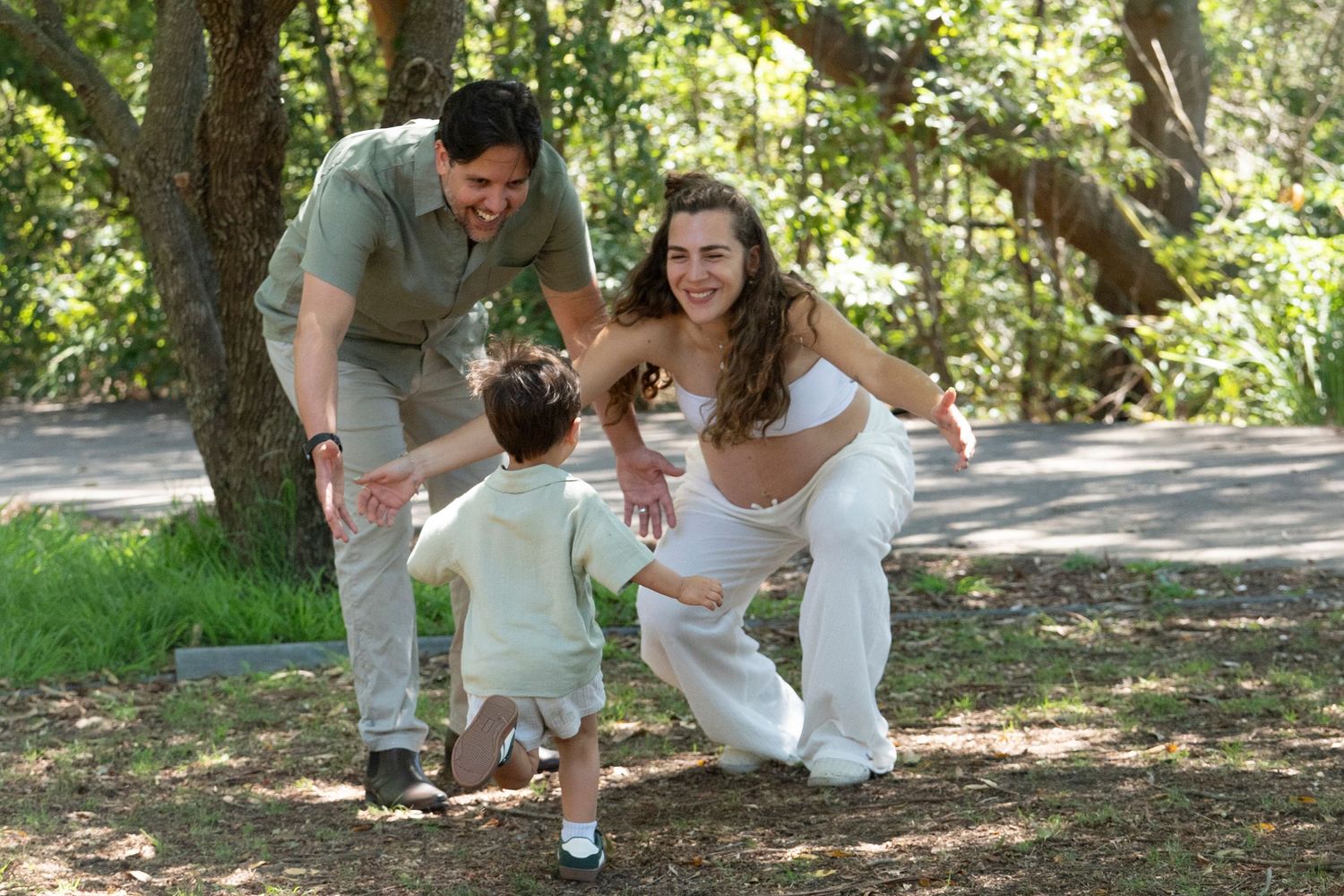 Family enjoying a playful moment together on a sunny path surrounded by green trees and nature.