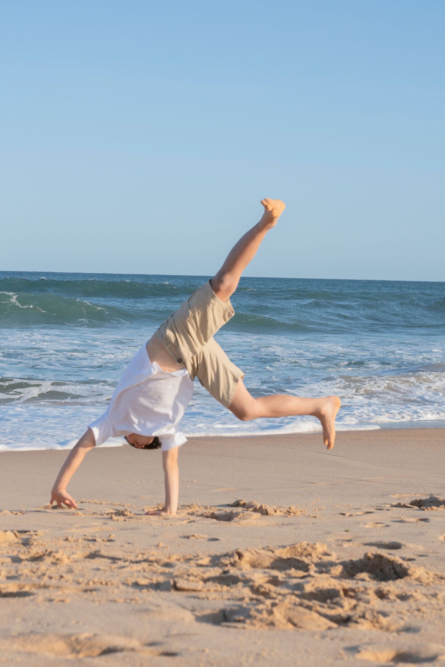 Person doing a cartwheel on a sunny beach with ocean waves in the background.