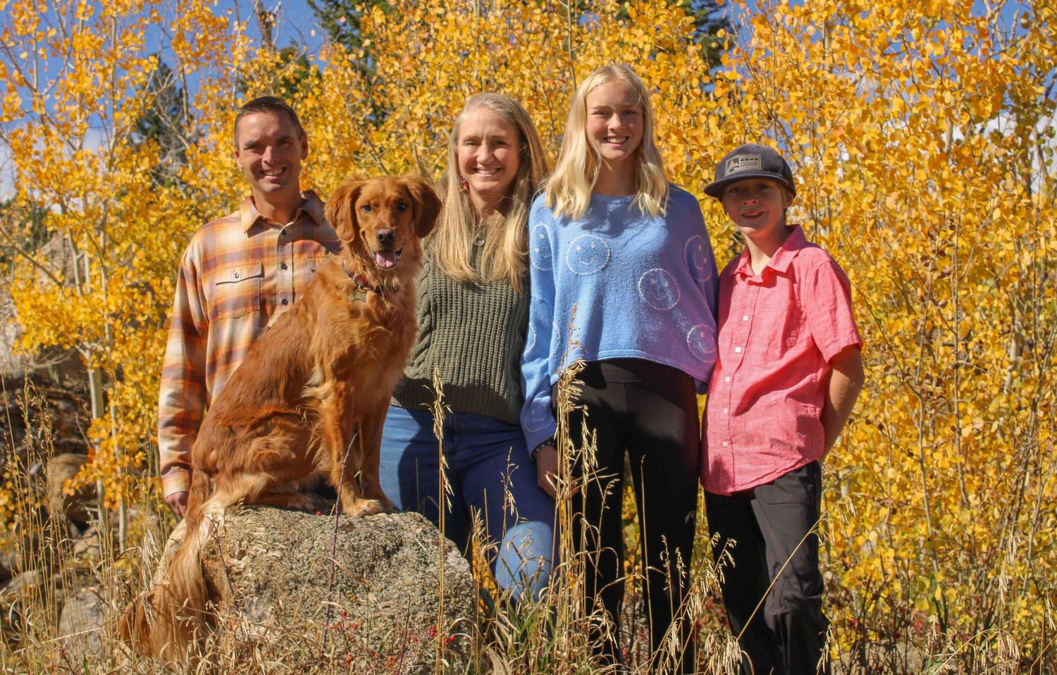 A group stands together on a rocky outcrop against vibrant yellow autumn aspen trees in the background.