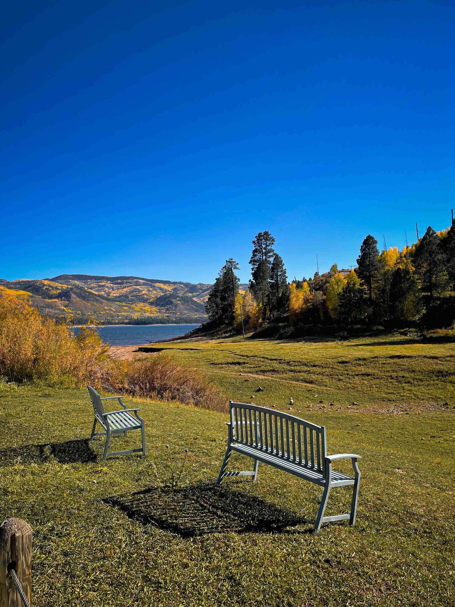Two benches overlooking a serene lake surrounded by autumn trees and mountains.