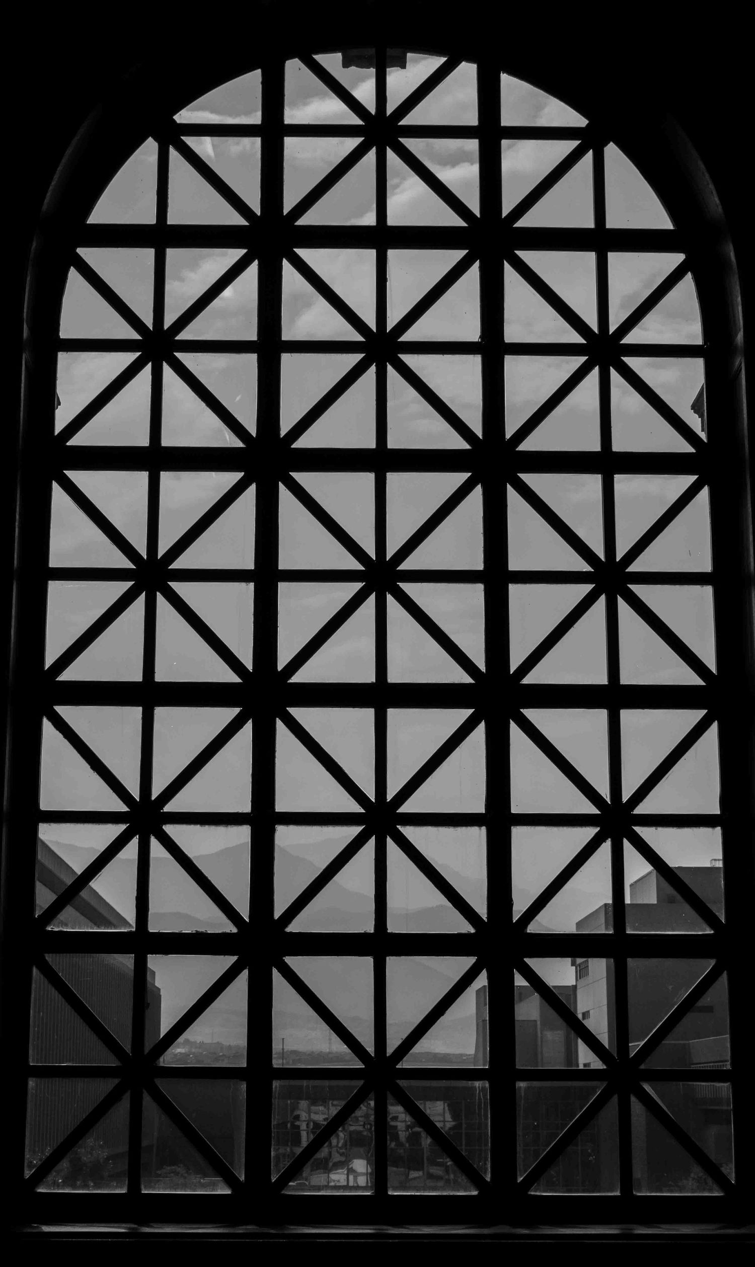 Geometric window lattice pattern creates dramatic shadows and silhouettes in black and white.