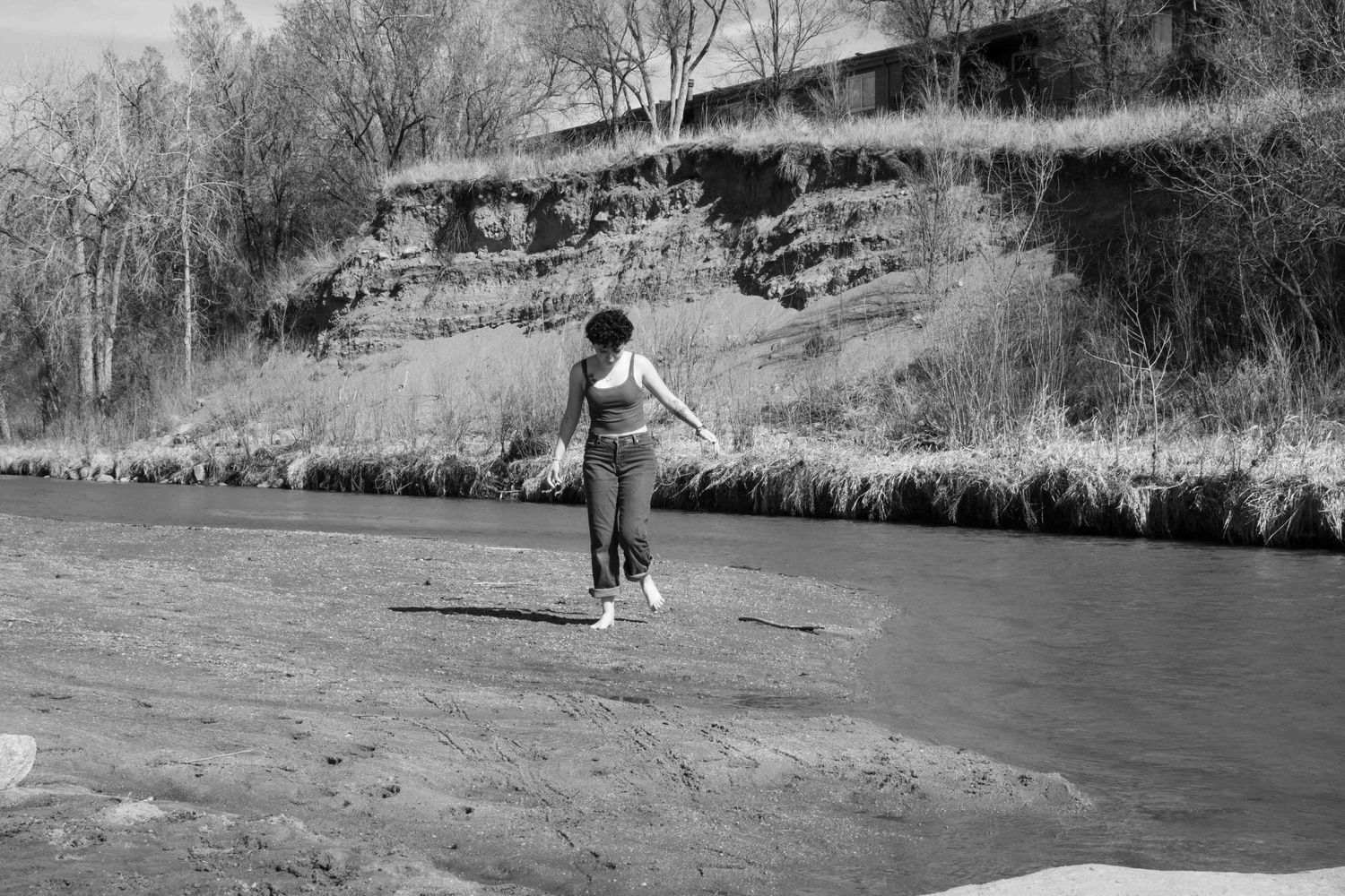 A person standing near a riverbank on a black and white landscape.
