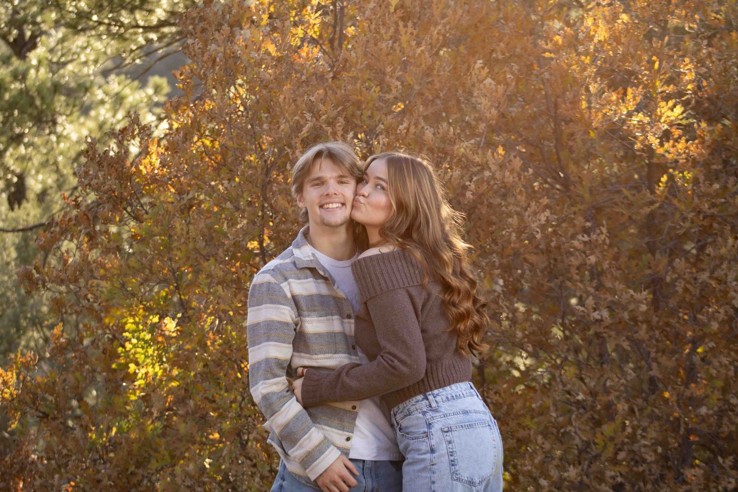 A tender moment between a couple captured in warm sunlight with autumn foliage in the background.