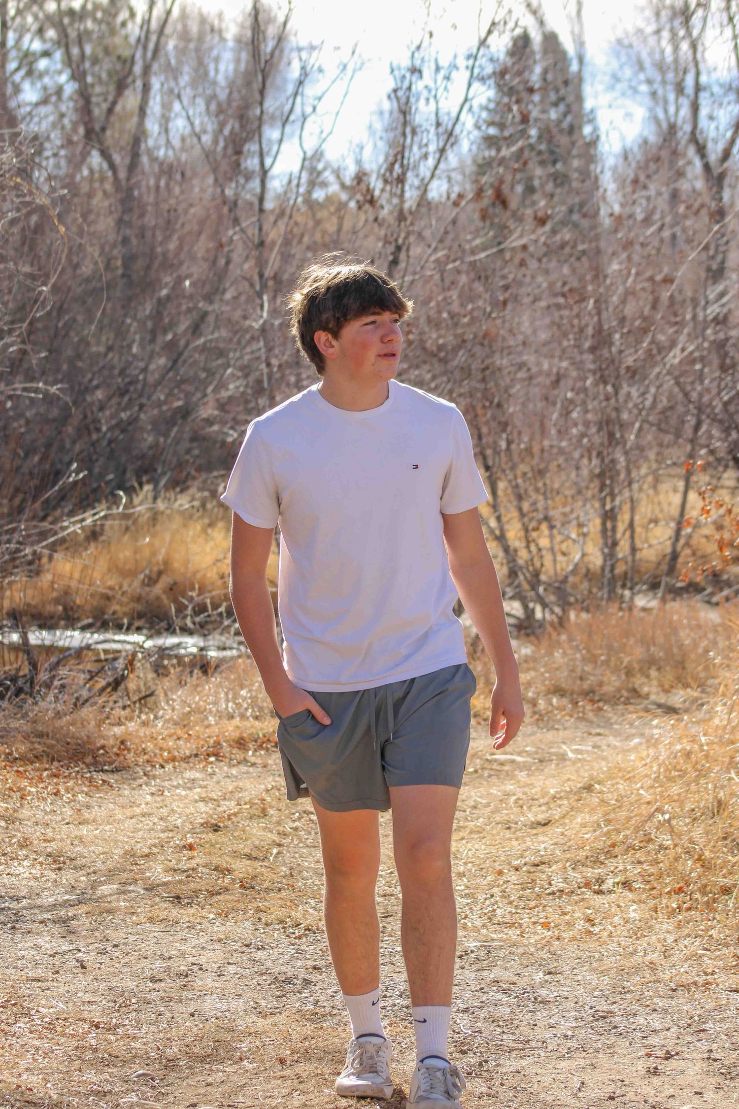 Someone walking on a dirt trail wearing a white t-shirt and shorts on an autumn day.