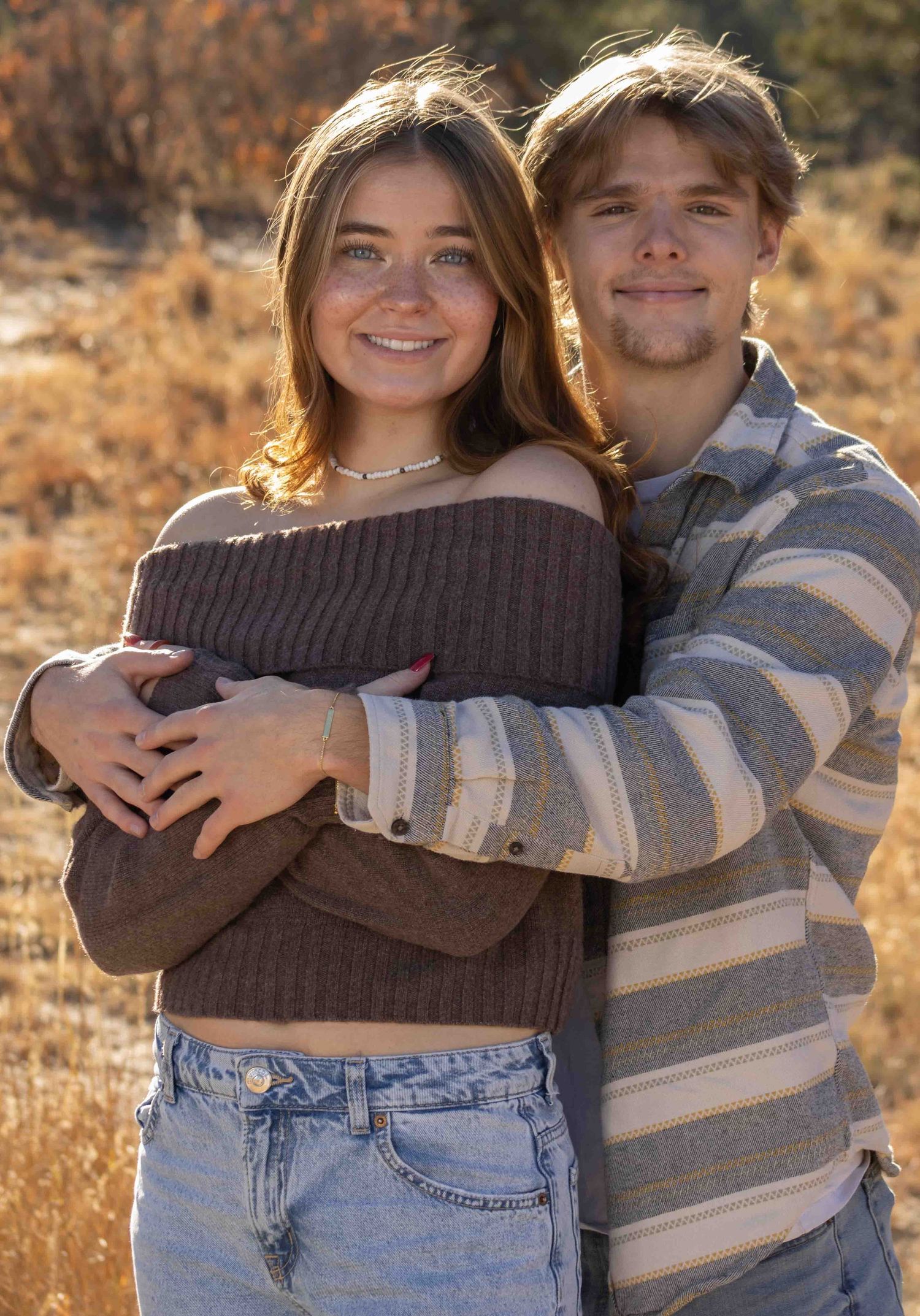 A romantic couple embraces in autumn sunlight, wearing casual sweaters against a golden backdrop.