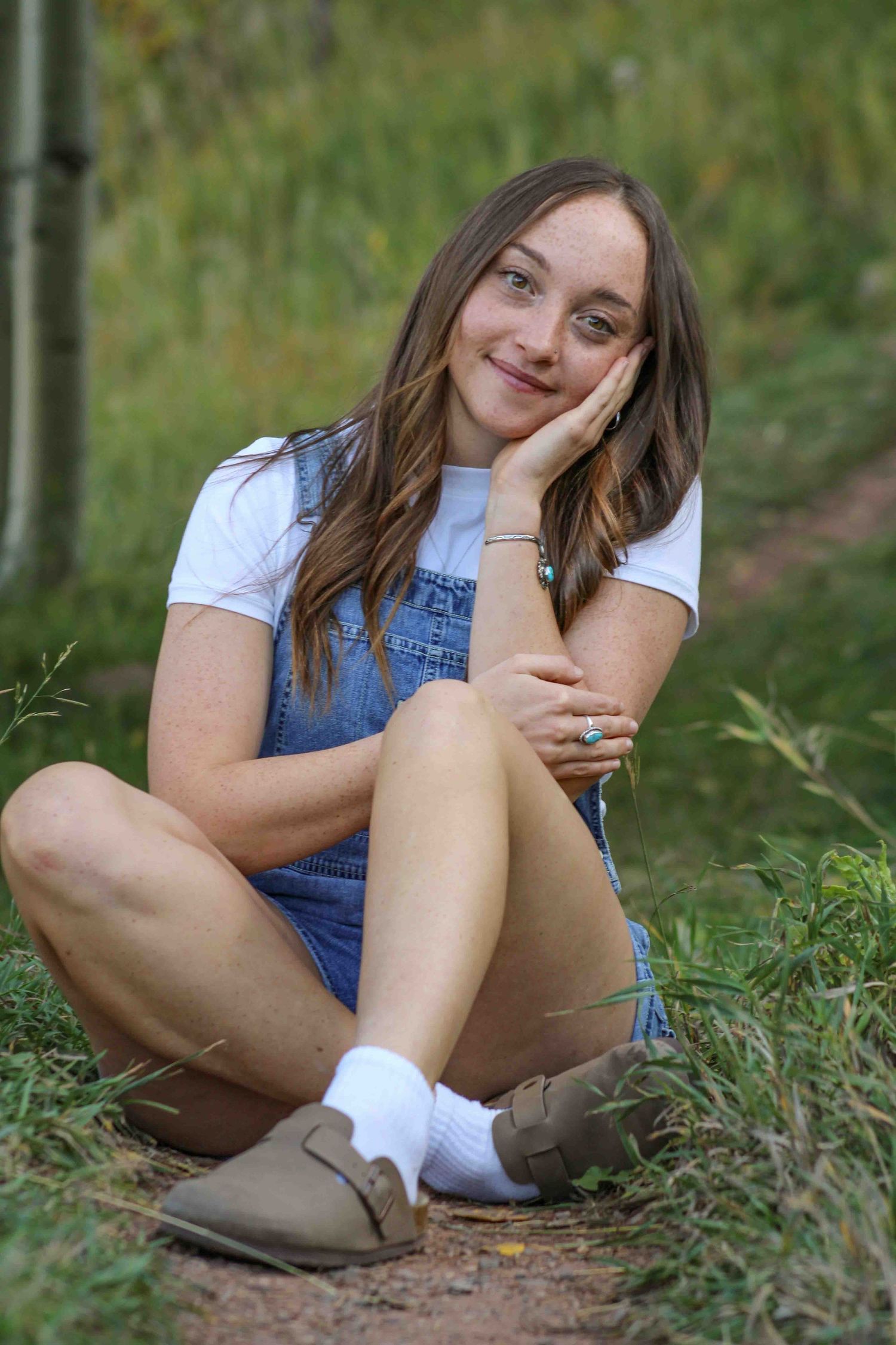 Person in denim overalls sitting casually on outdoor trail.