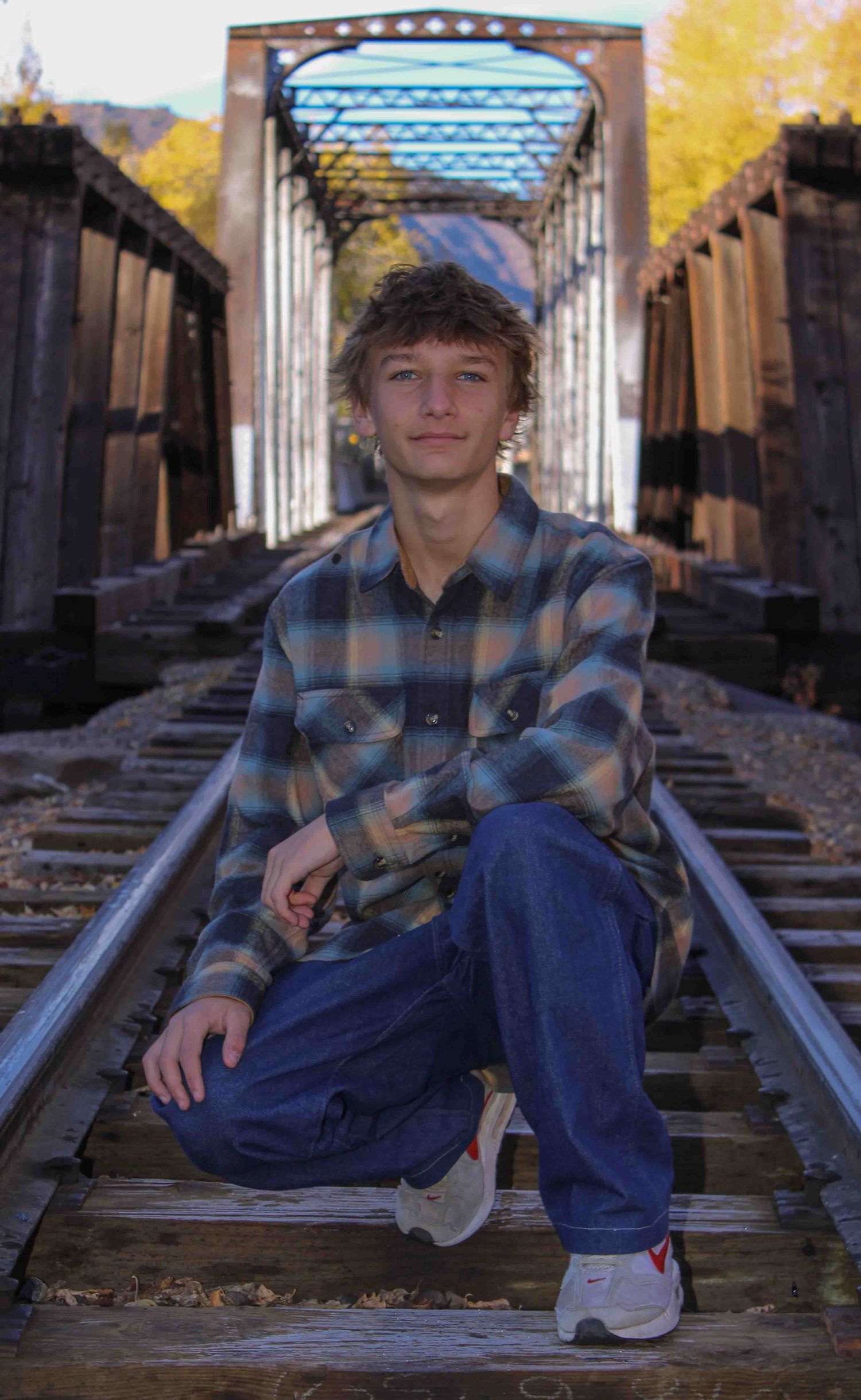 Someone in a plaid flannel shirt and jeans poses on railroad tracks beneath a covered bridge in autumn.