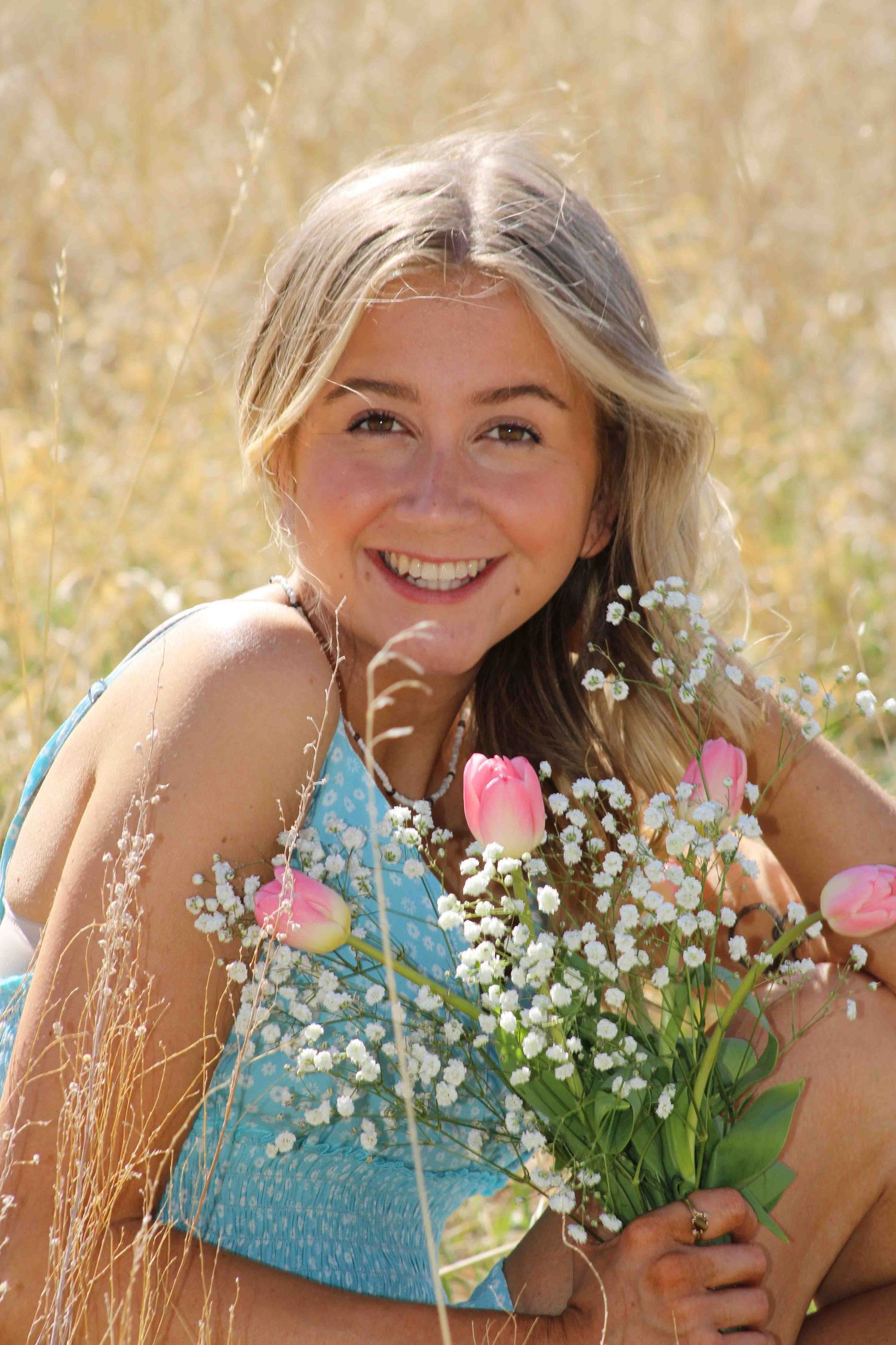Someone posing in a meadow with baby's breath flowers and pink tulips in summer sunshine.