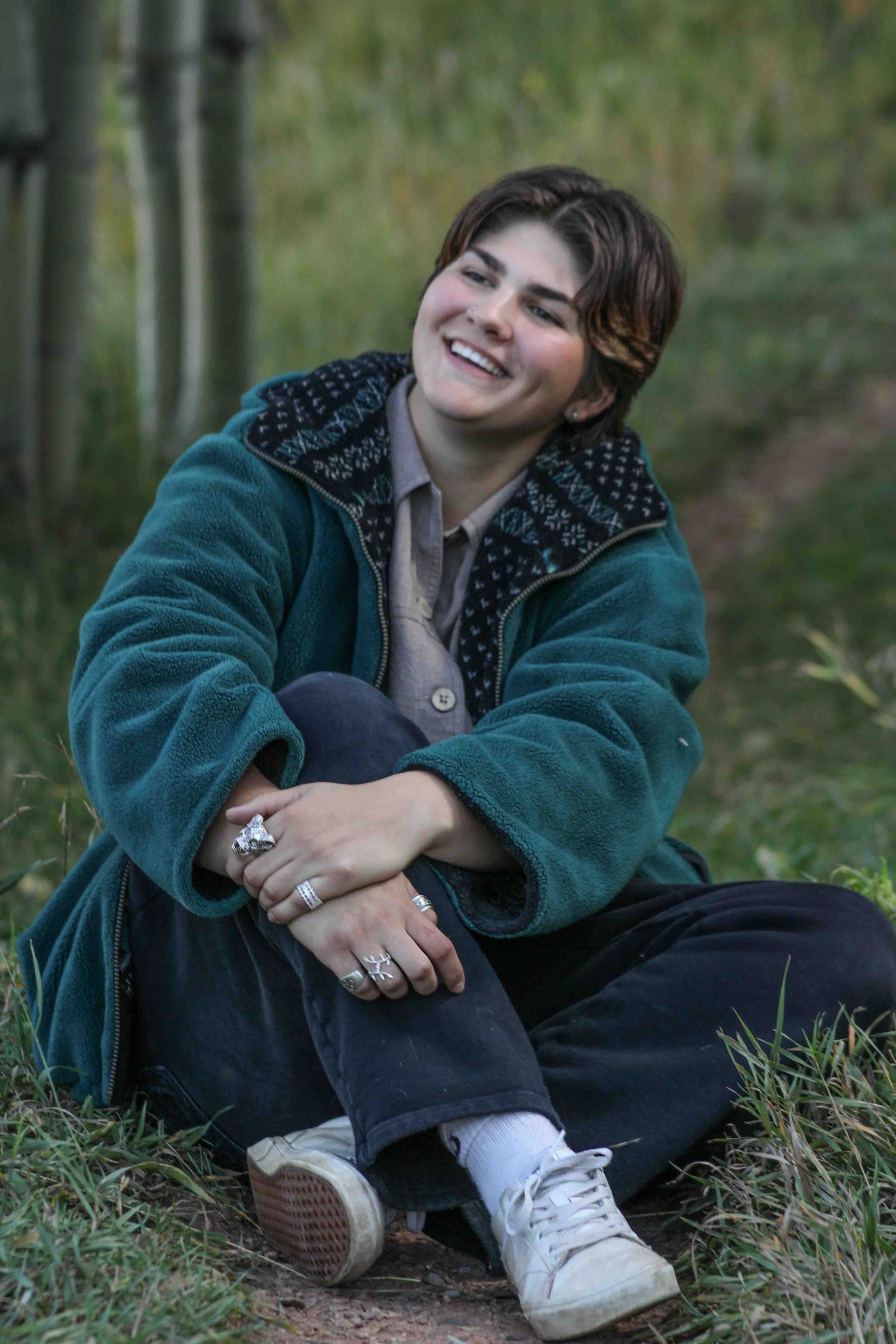 Person in green coat sitting casually outdoors among aspen trees.