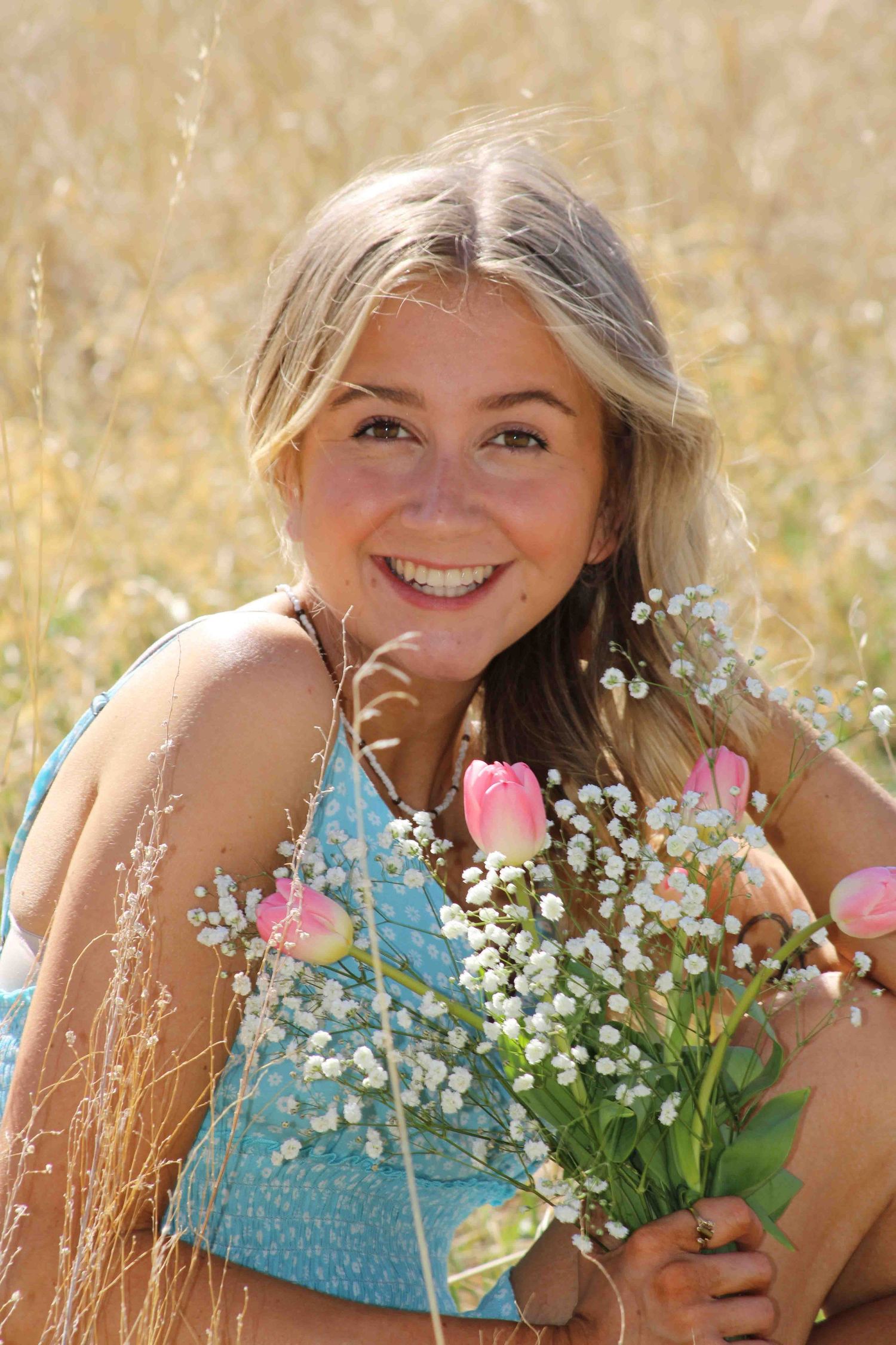 A joyful portrait in a summer field holding a bouquet of pink tulips and baby's breath against a golden wheat backdrop.