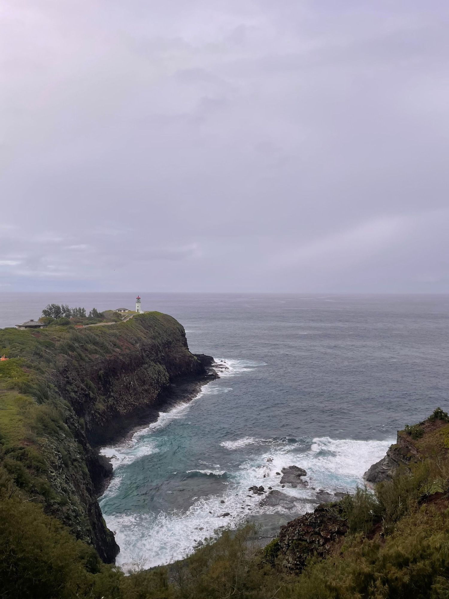 A lighthouse stands on dramatic coastal cliffs above crashing ocean waves.