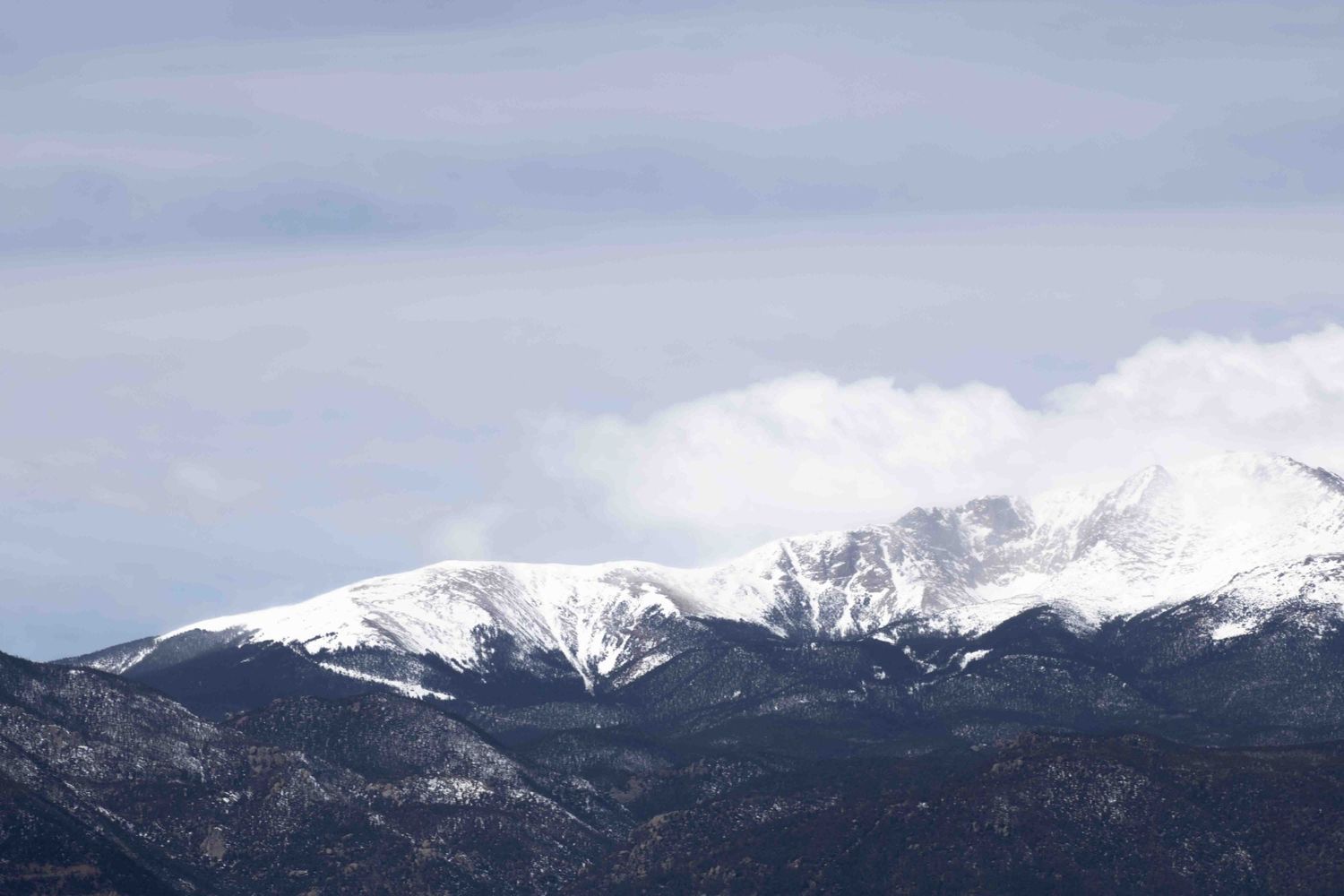 Majestic snow-covered mountain range with cloudy sky backdrop.