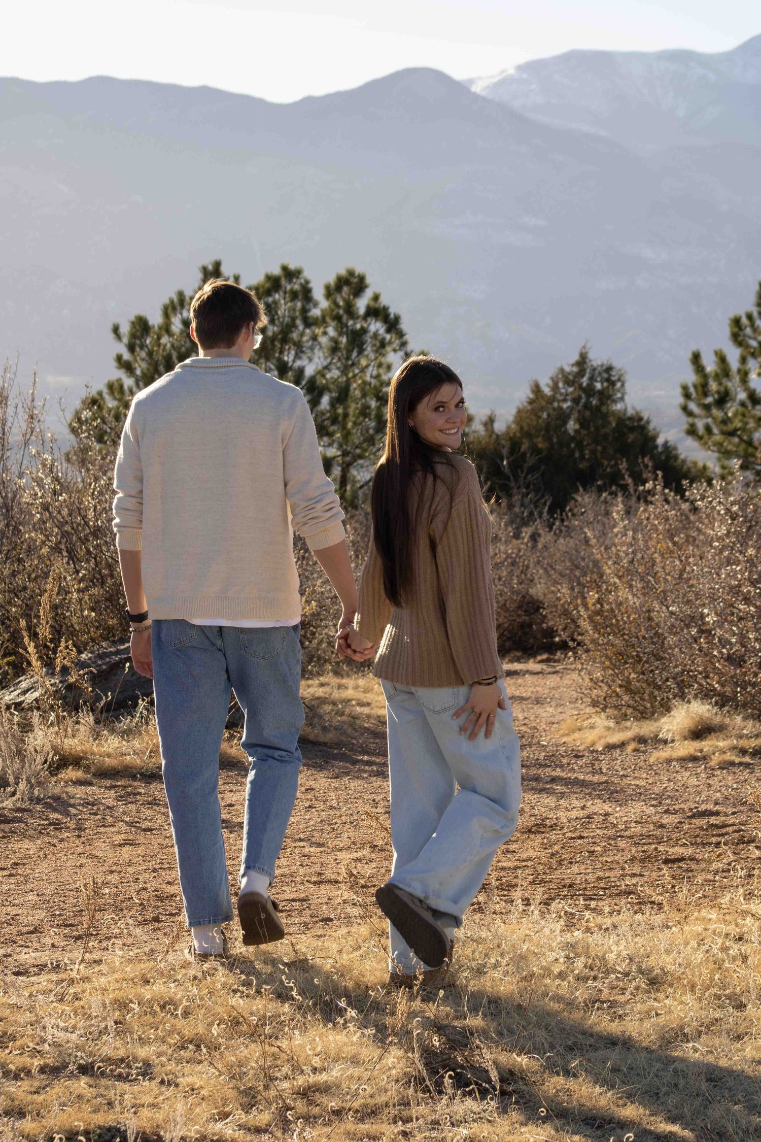 Two people in matching outfits walk through desert landscape with mountains in background.
