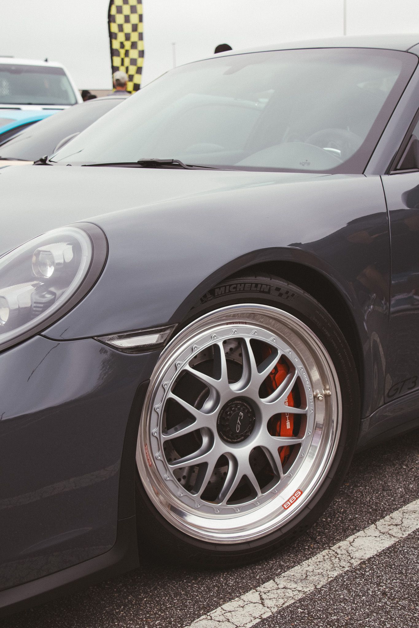Silver Porsche sports car wheel detail showing BBS mesh style rim and red brake caliper.