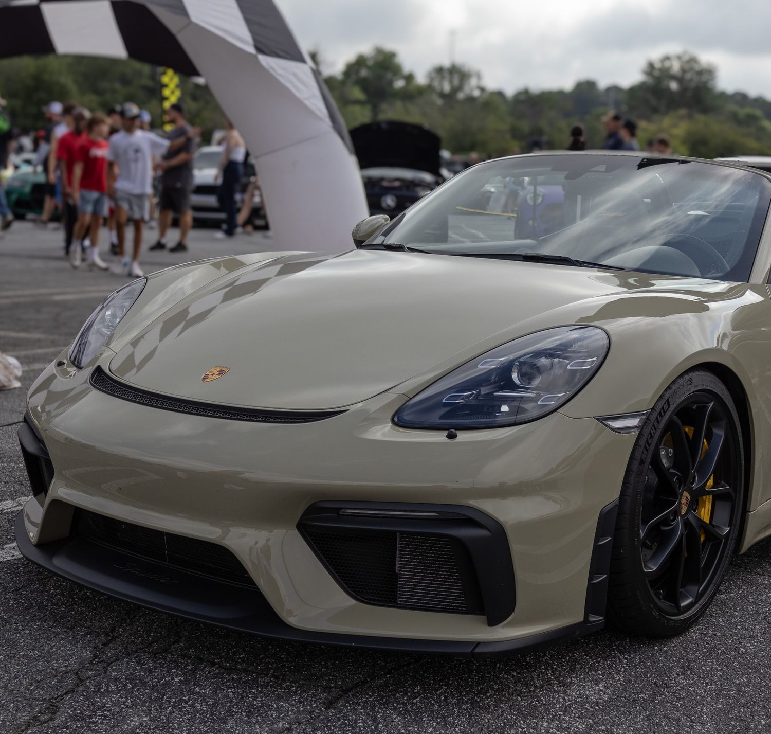 Cream-colored Porsche Cayman GT4 with black wheels and distinctive front splitter.