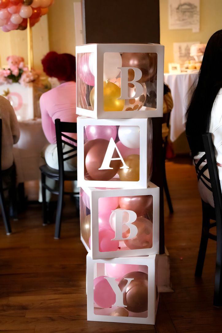 Decorative white BABY blocks display with pink balloons at baby shower celebration.