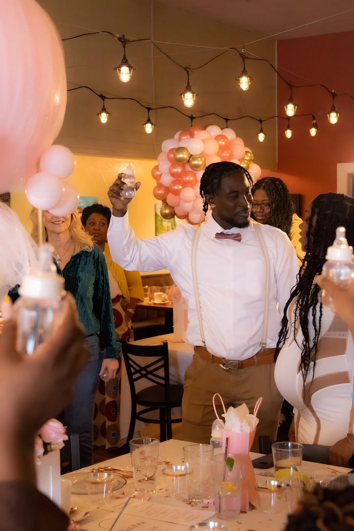 Celebration at party venue with string lights and pink balloons as guest raises glass for toast.