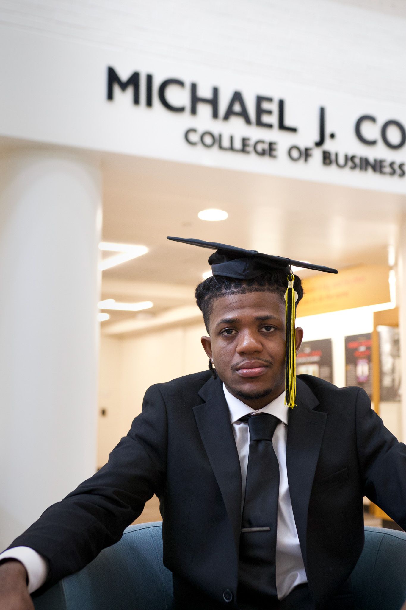 Graduate in cap and gown seated at Michael J. Co College of Business.