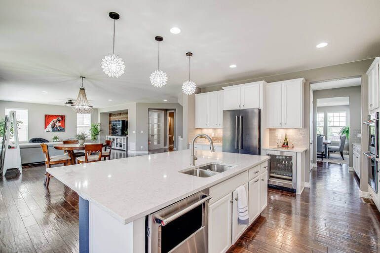 Modern open concept kitchen with white cabinets, quartz countertops, spherical pendant lights and hardwood floors.