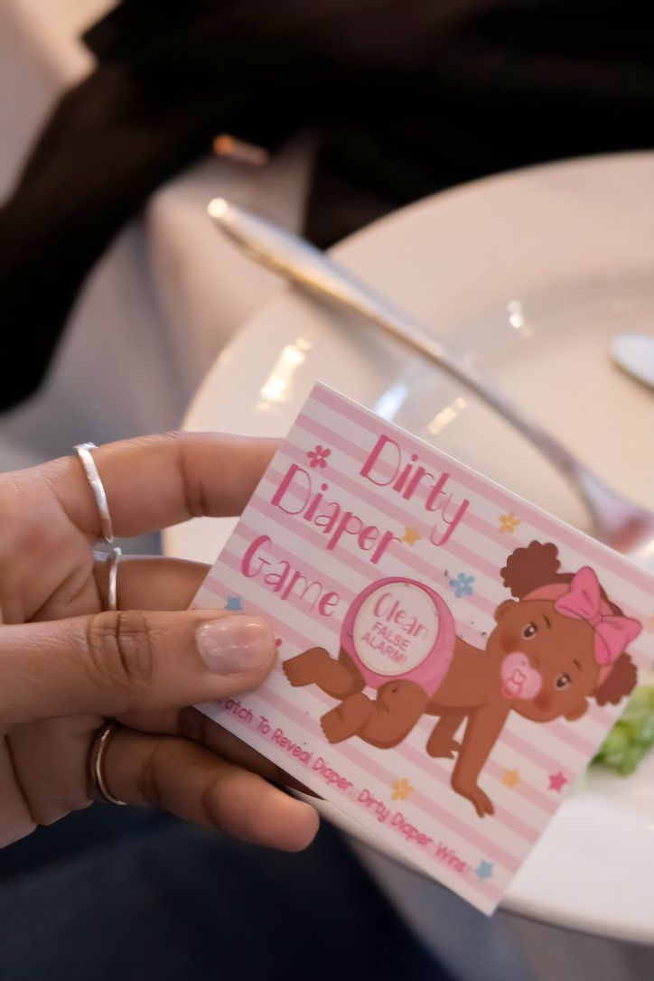 Hand holding pink dirty diaper game card at baby shower party.