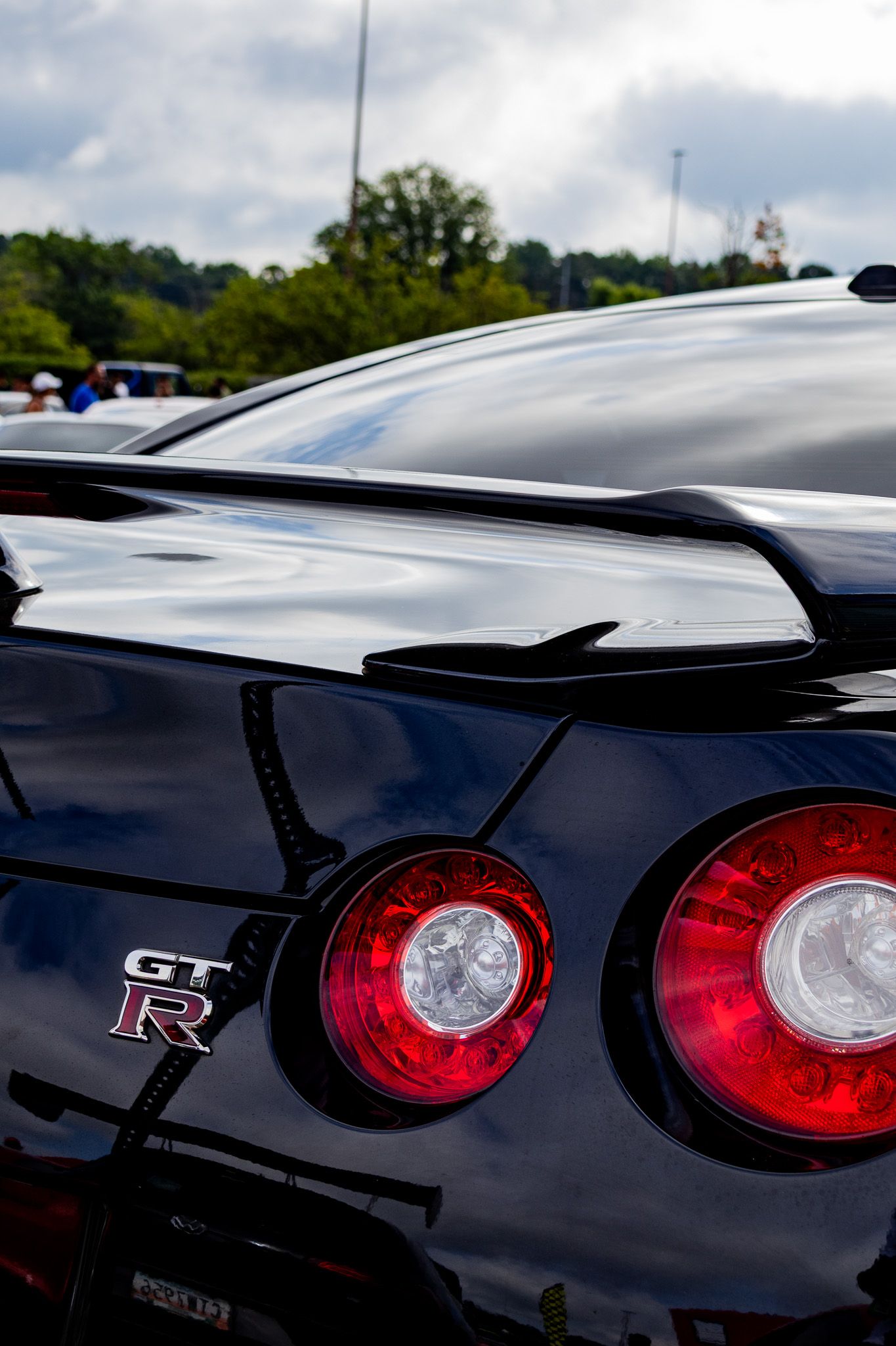 Close up of a black Nissan GTR rear end showing iconic round tail lights and spoiler details.