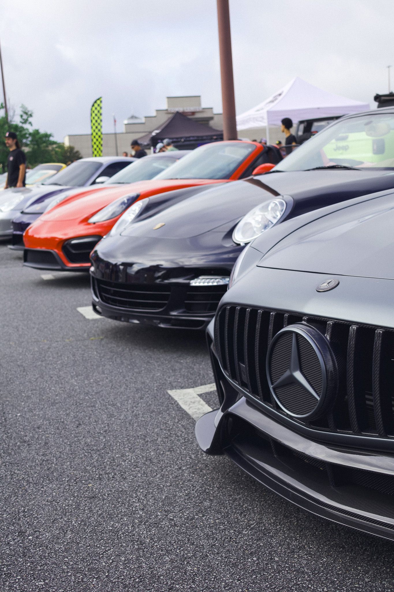 Row of luxury sports cars including Mercedes and Porsche models lined up at an outdoor event.