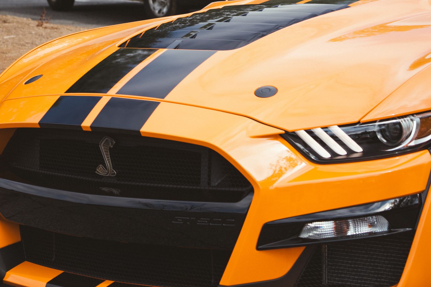 Close up front view of orange Ford Mustang GT500 showing aggressive hood and headlight design.