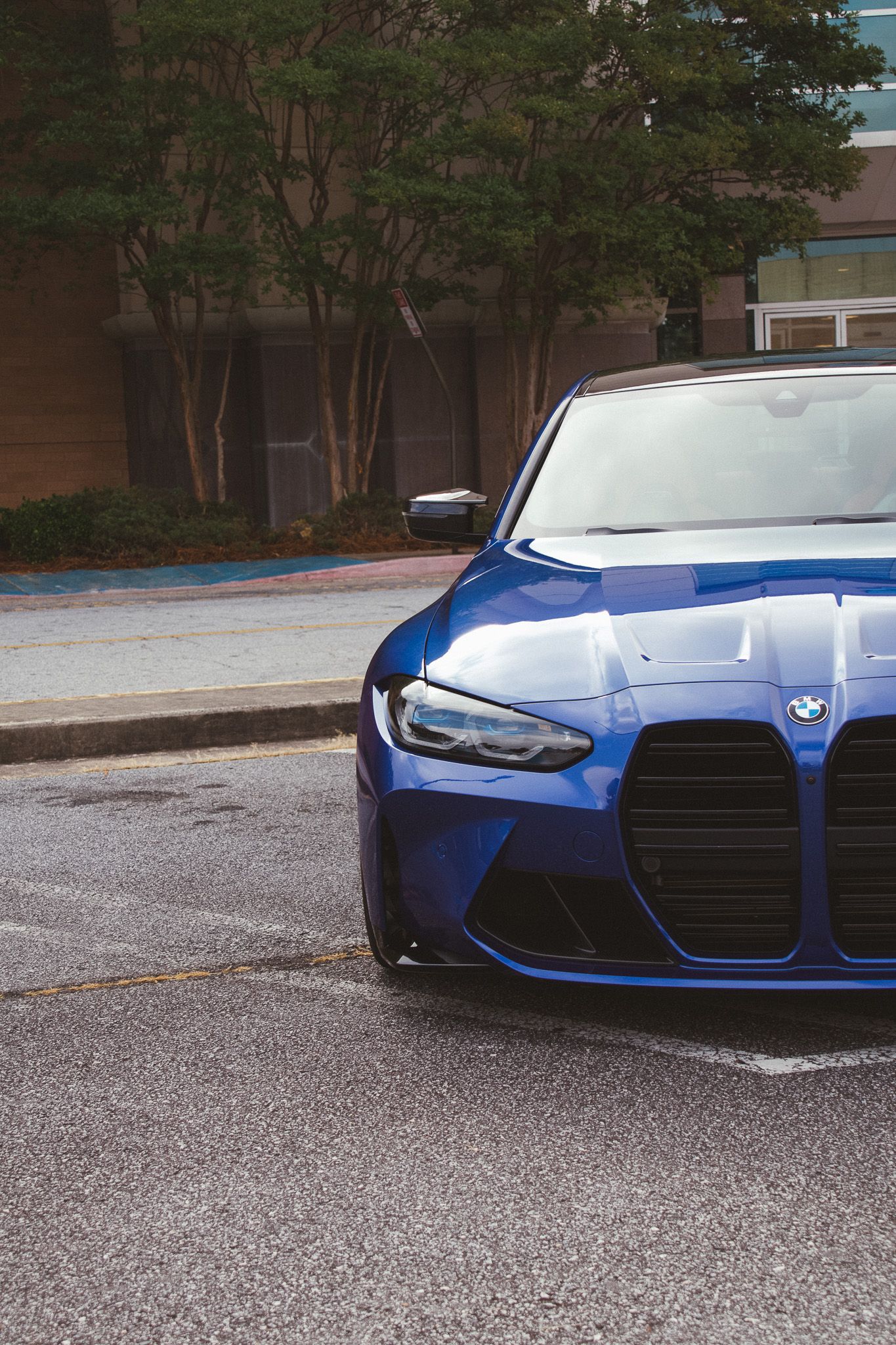 Front quarter view of a blue BMW M4 showing the large signature kidney grille design.